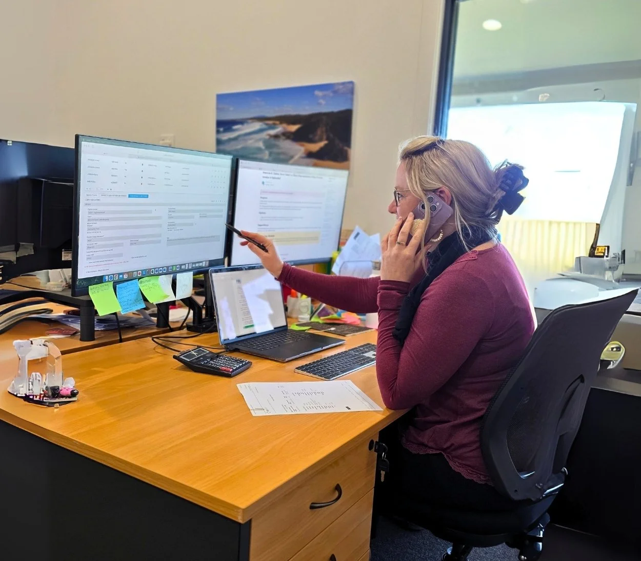 A woman sitting at a computer desk, talking on the phone.