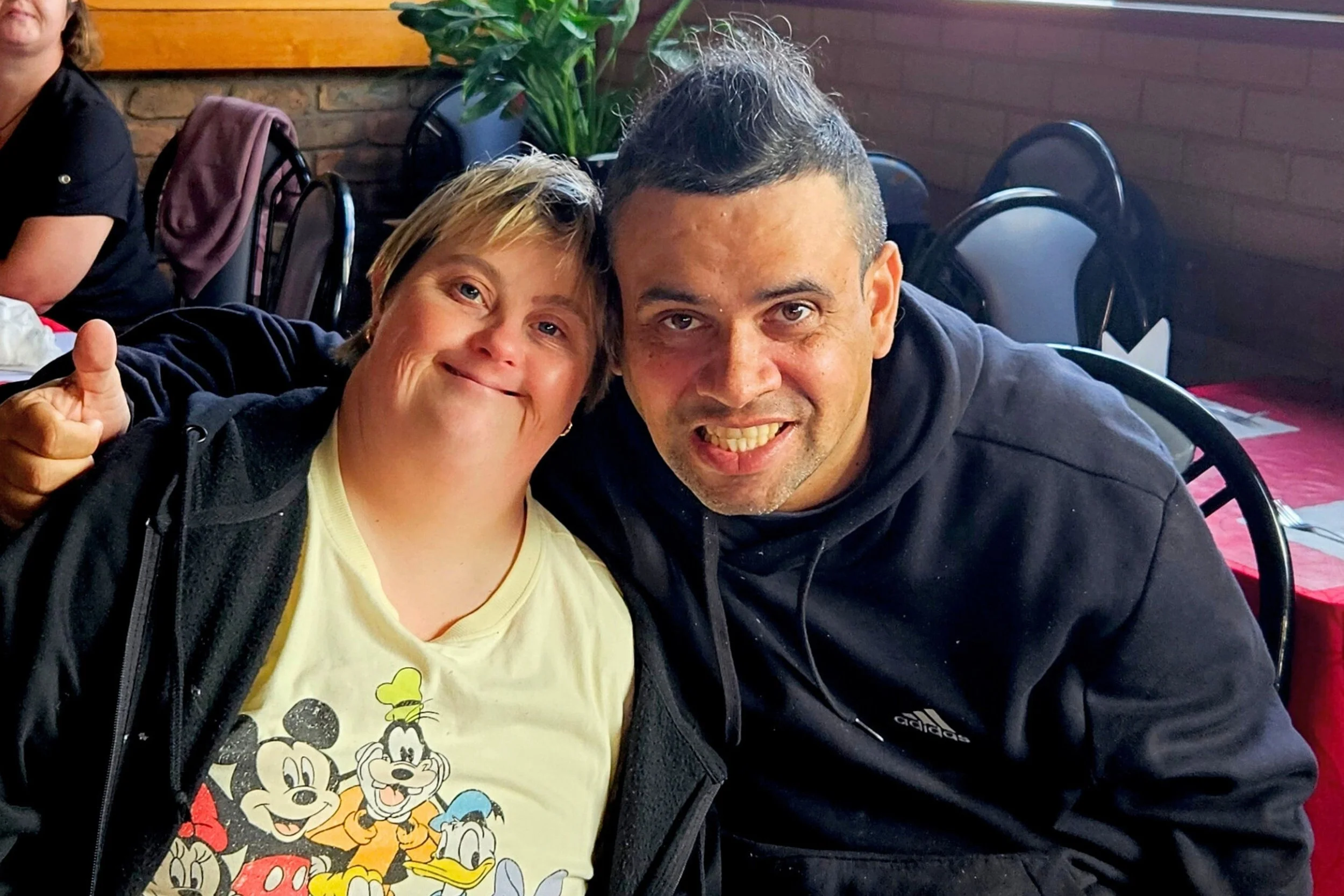 Two friends smiling and sitting close together at a restaurant during the Narooma Movies & Lunch outing