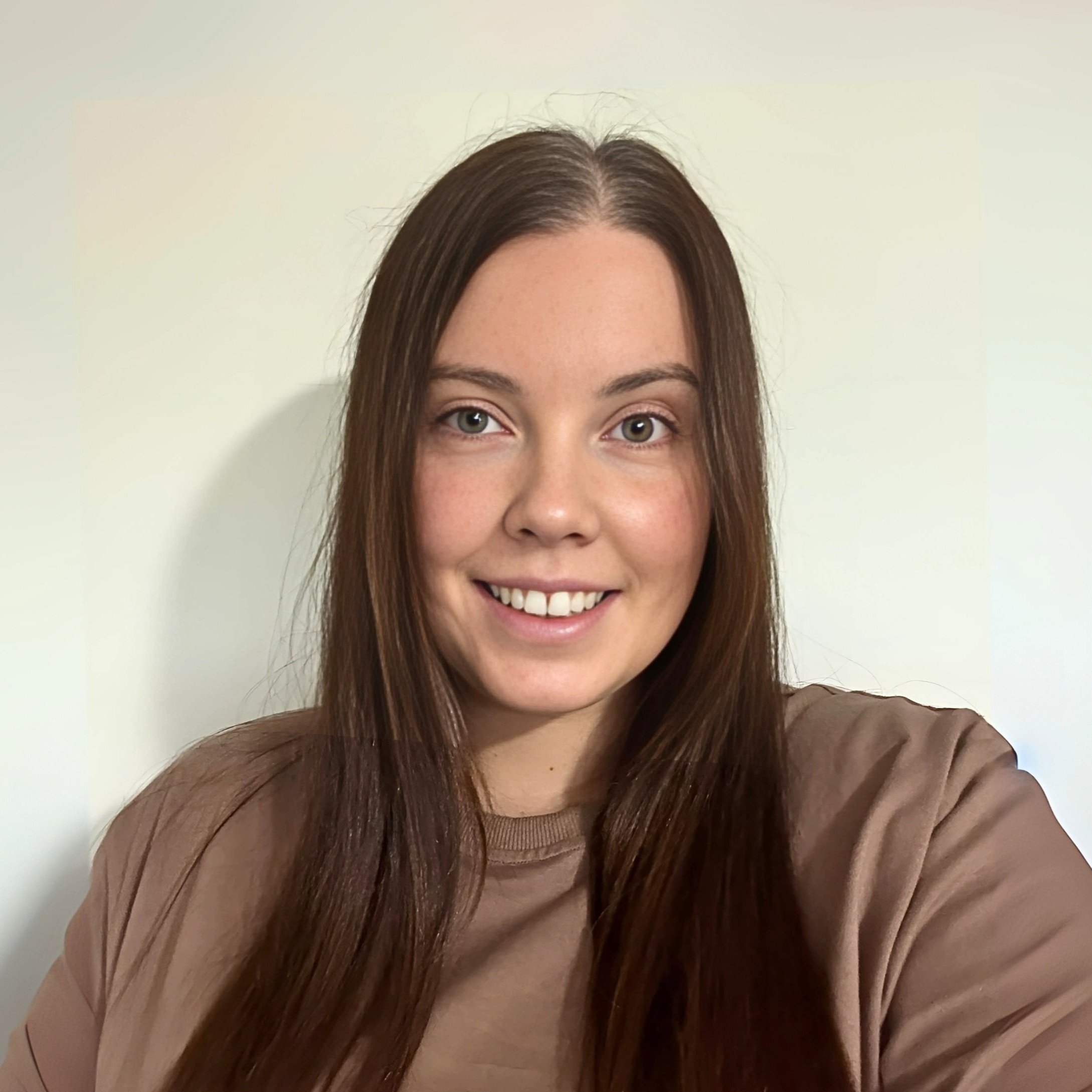 Image of Emma, Senior Support Coordinator woman with long brown hair taken in front of a plain white wall.