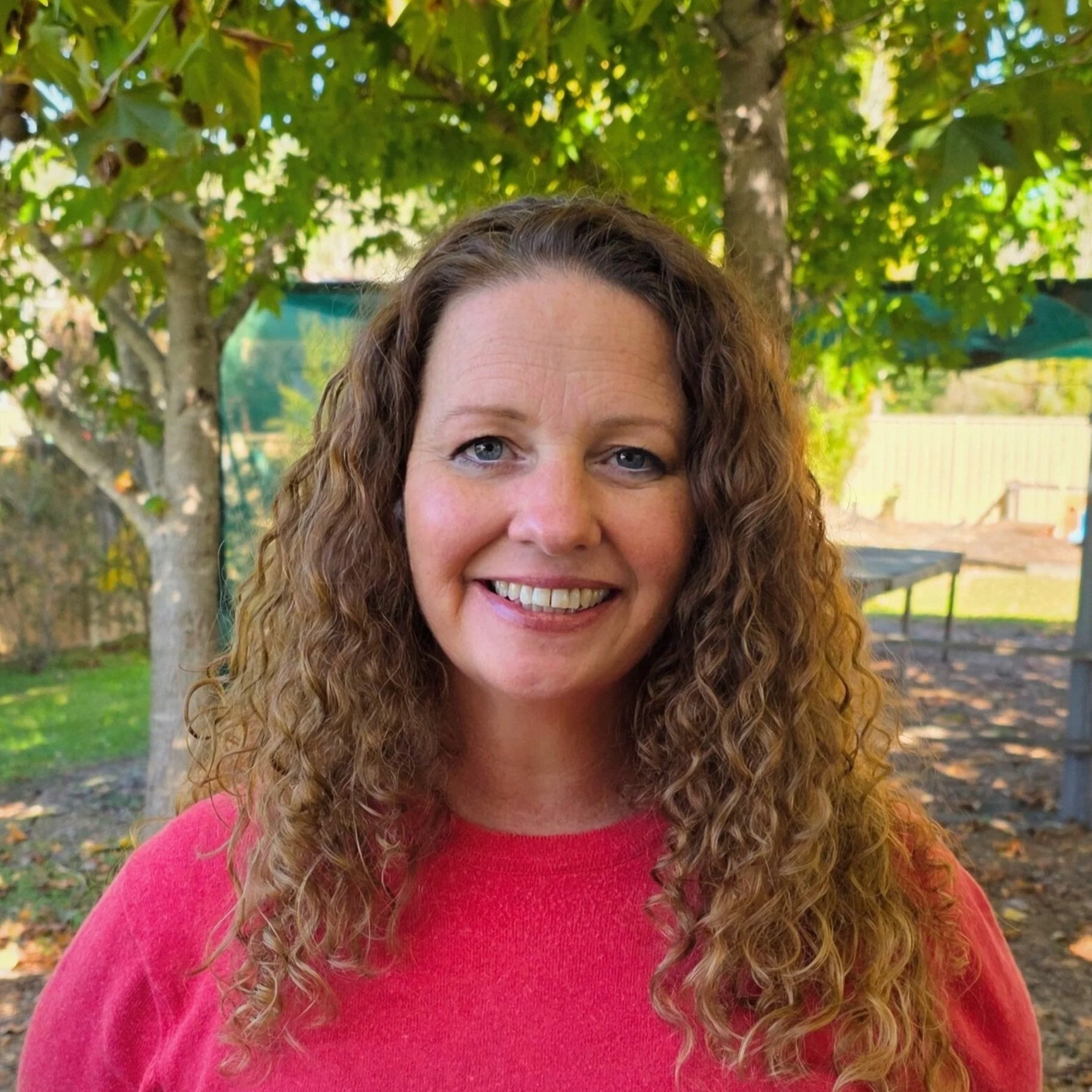 A woman with long, curly brown hair smiling outdoors.