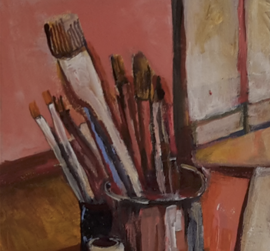 Paintbrushes in a mug on a table, with a pink wall and part of a window in the background.