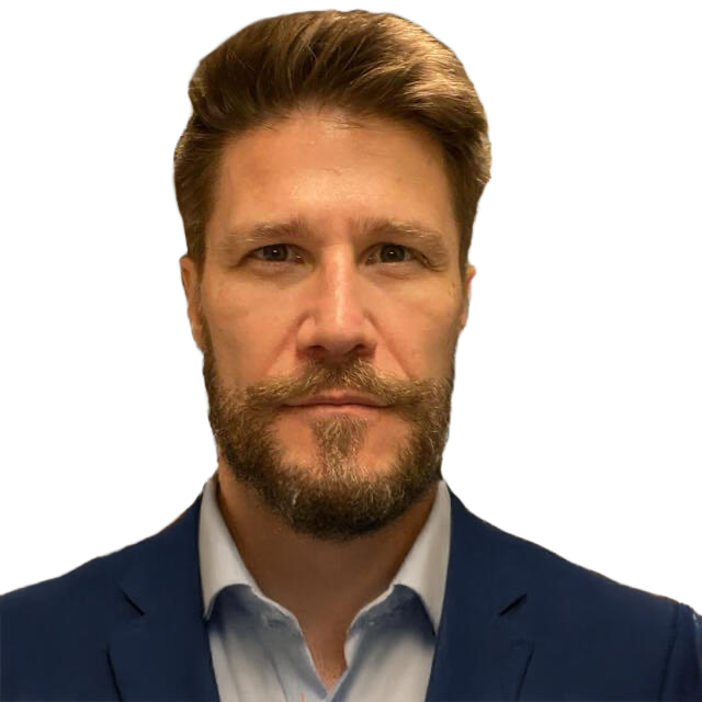 A man with brown hair and a beard wearing a blue suit and white shirt, looking directly at the camera.