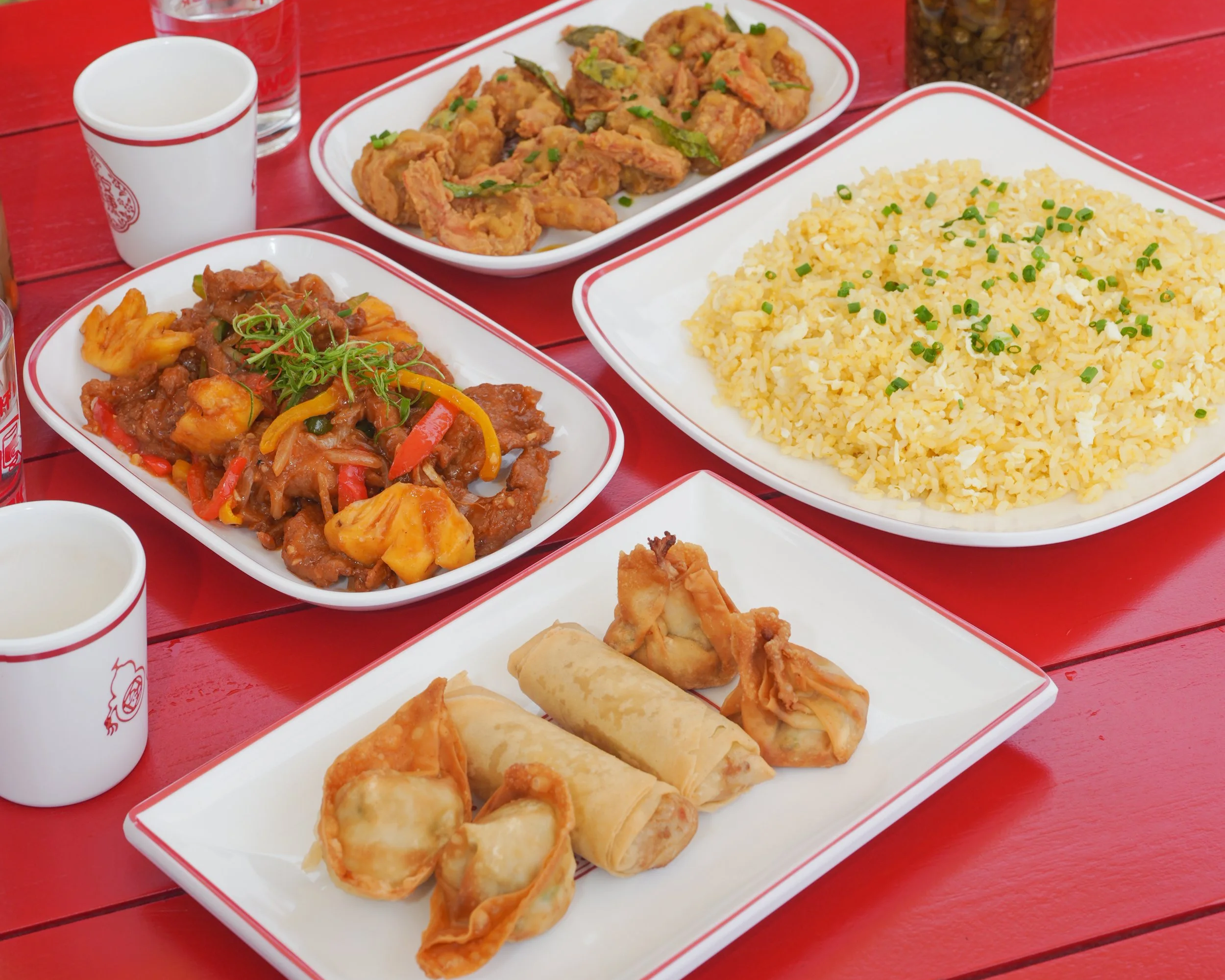 A vibrant outdoor spread of the best Chinese food in Canggu, featuring sweet and sour chicken, egg fried rice, spring rolls, and dumplings on a red table at Wok This Way Bali.