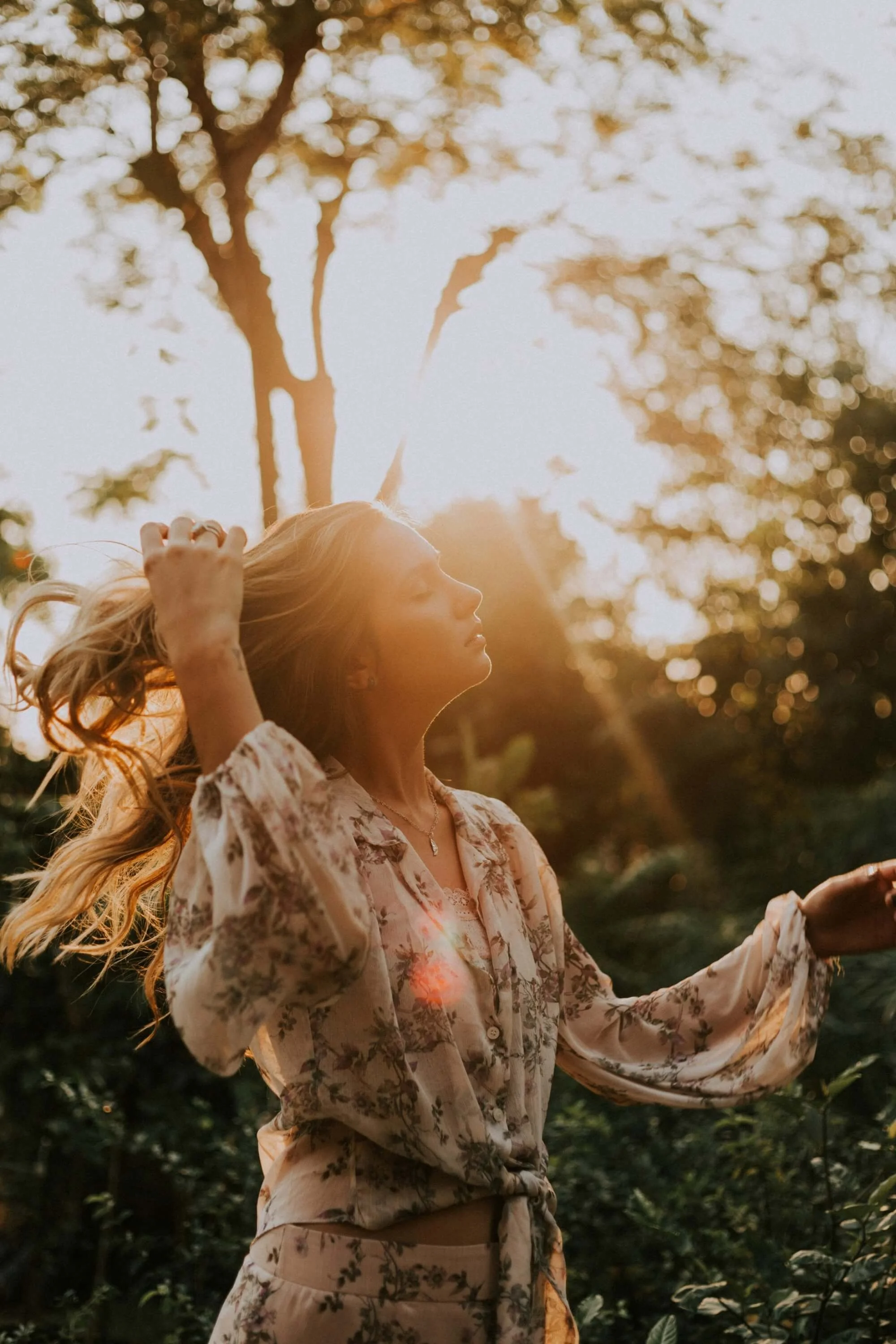 Nuori nainen häärää luonnossa auringon laskiessa, taustalla puita ja vihreitä kasveja.