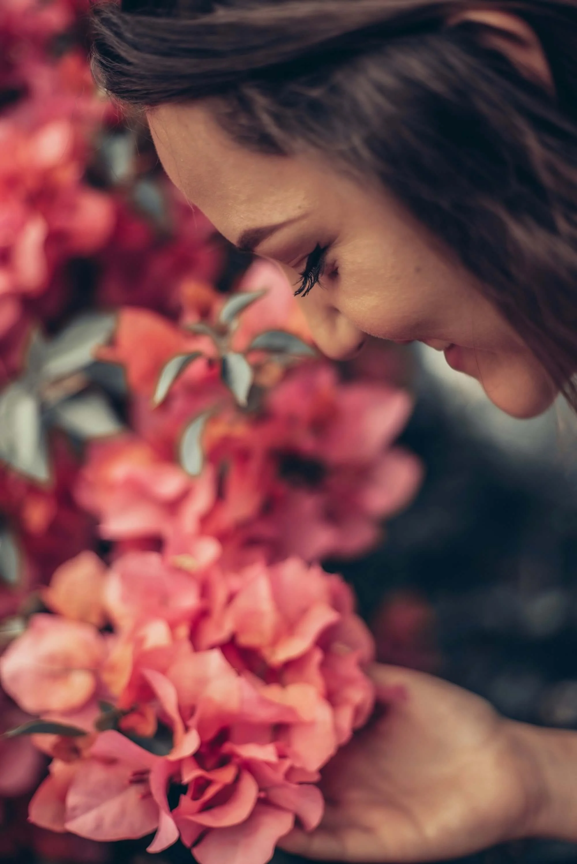 Nuori nainen tuoksuttelee pinkkejä ja punaisia kukkia.