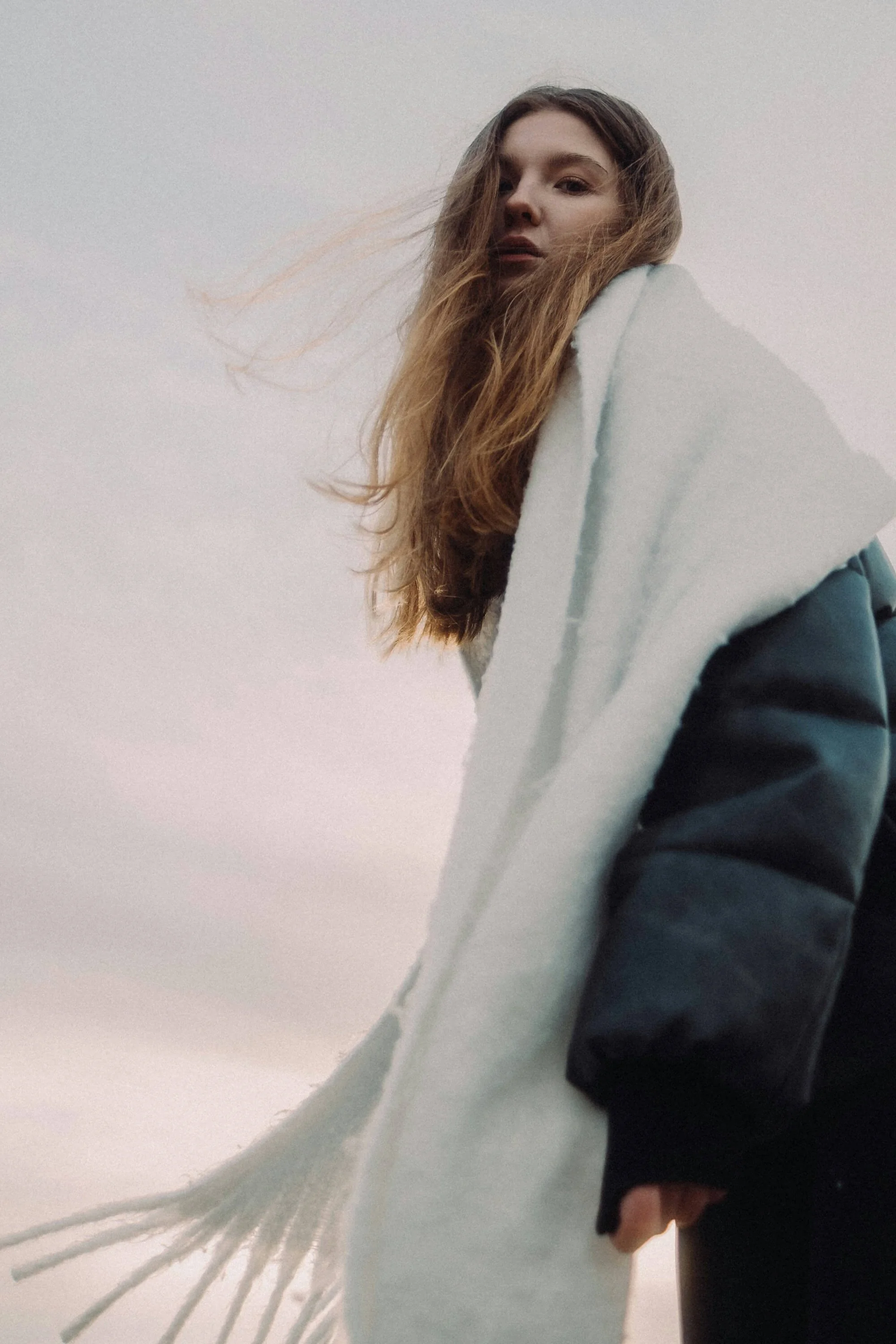 Nuori nainen katsoo kameraan, pilvinen taivas ja tuulenvire.