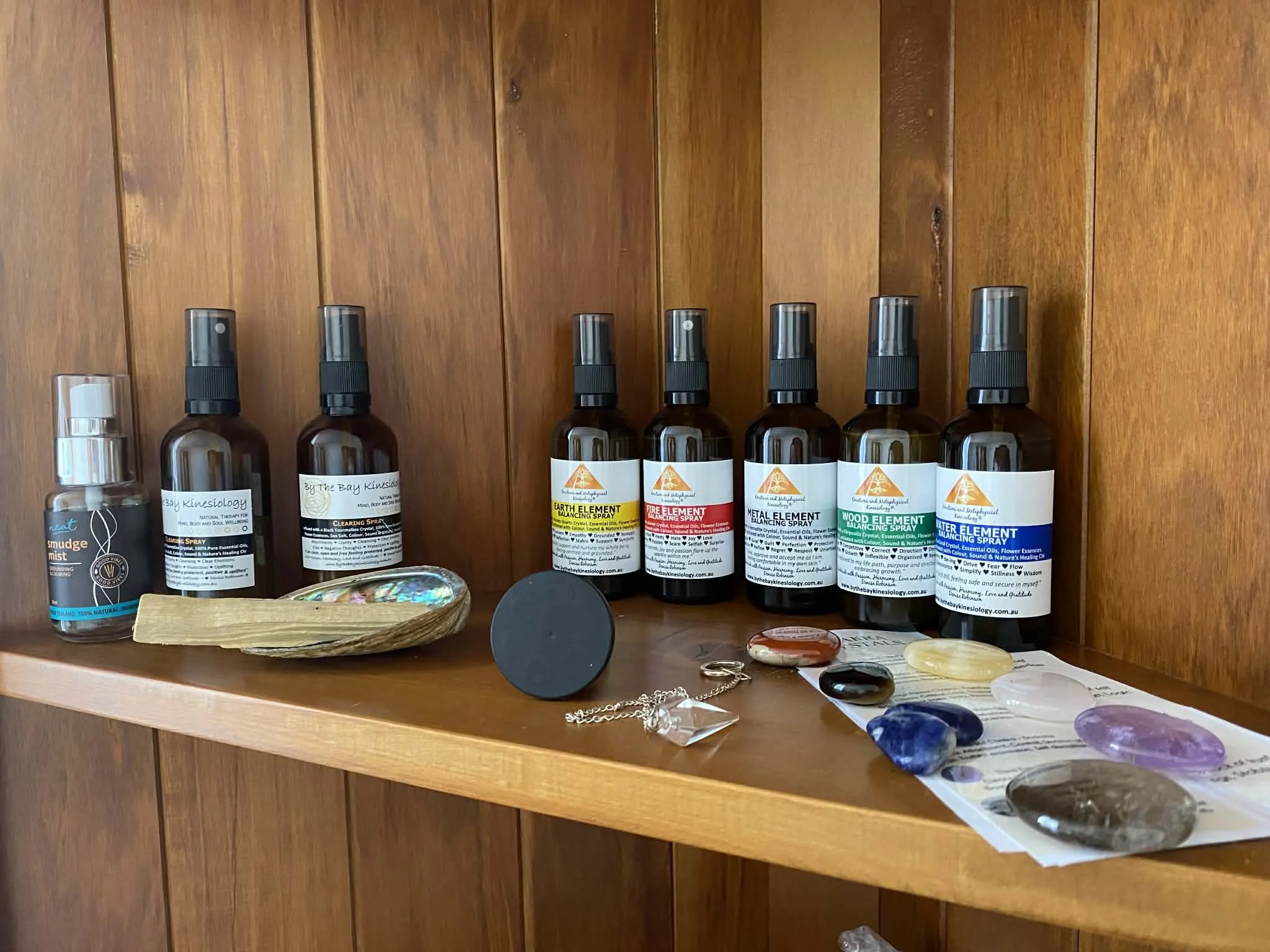 A wooden shelf displaying various spray bottles, small stones, jewelry, and other small decorative items.