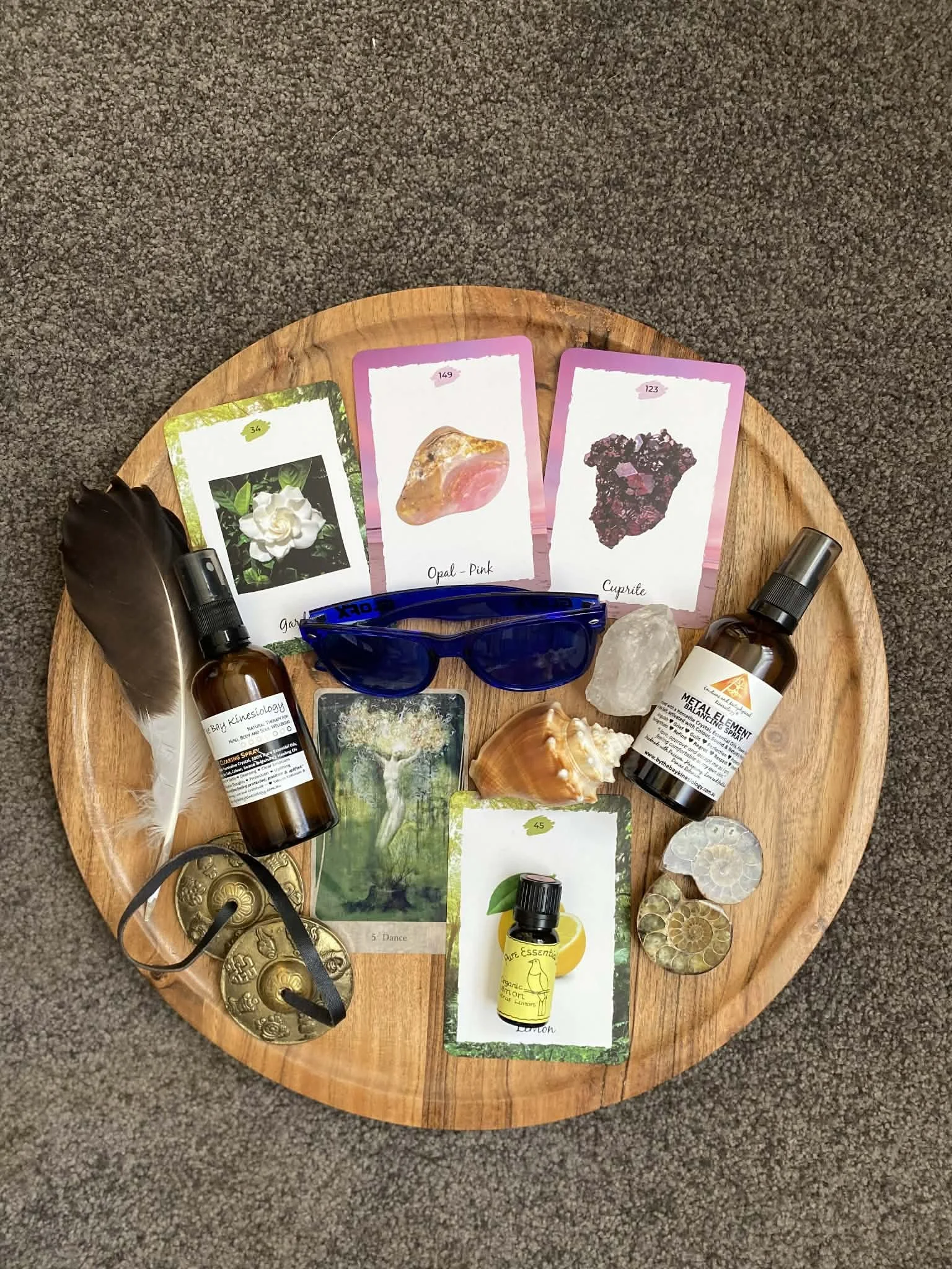 Round wooden tray with crystals, tarot cards, essential oils, and decorative metal coins on a carpeted floor.