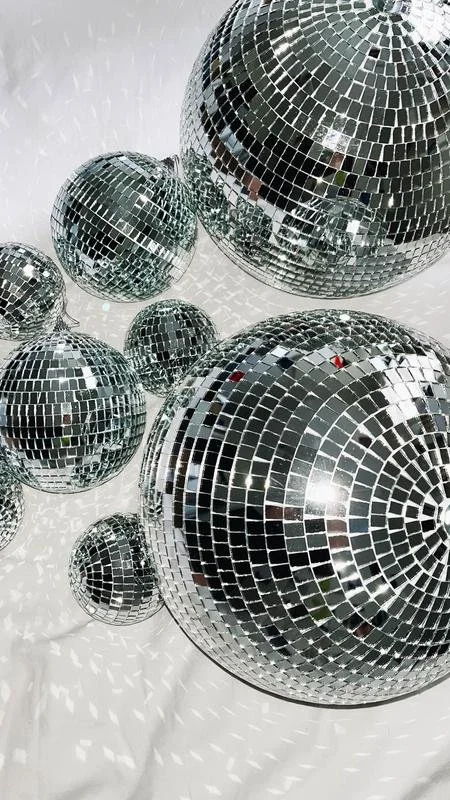 Multiple silver disco balls of various sizes reflecting light on a white background.