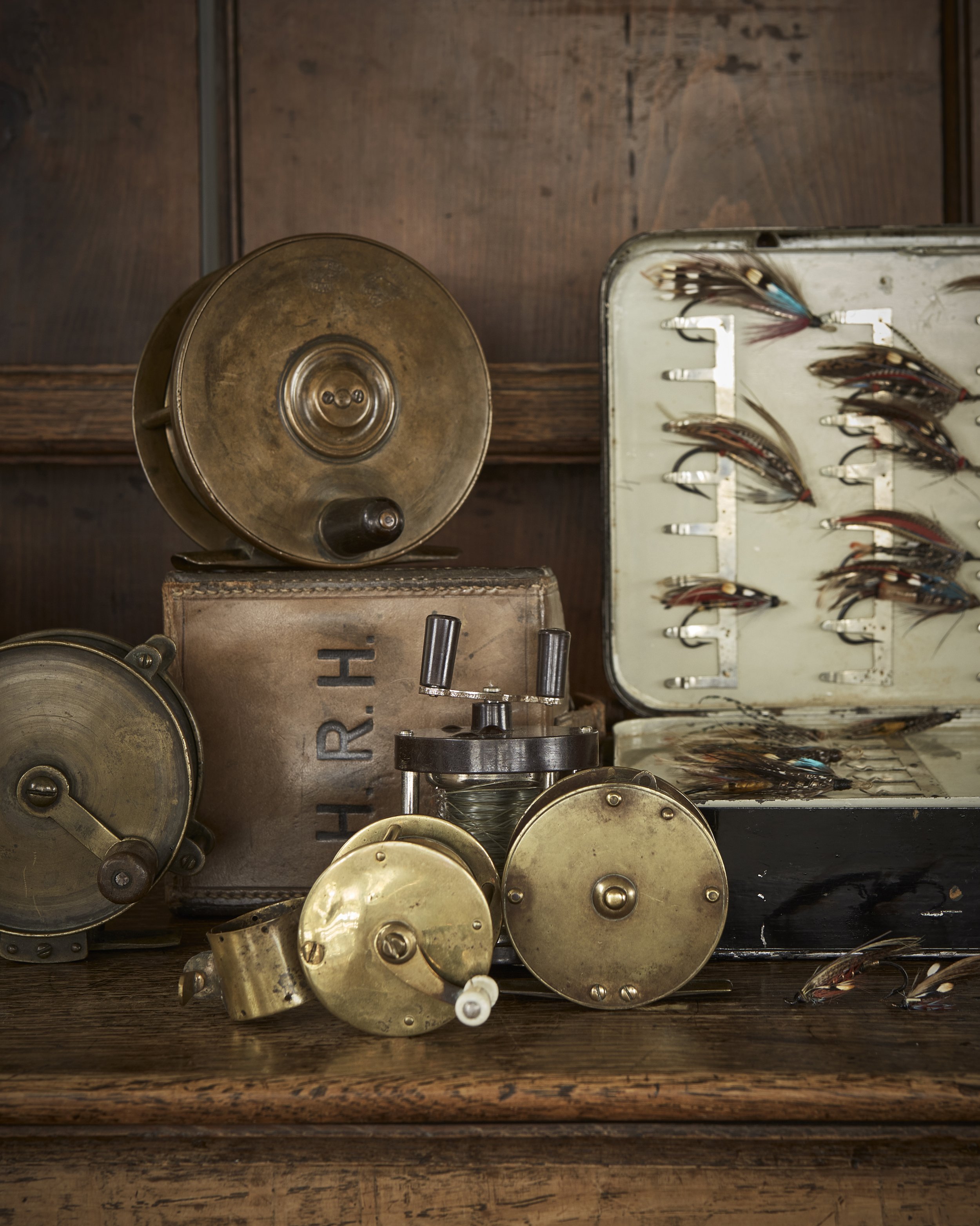 Old fishing tackle and reels on a wooden surface, with a box of fishing lures in the background.