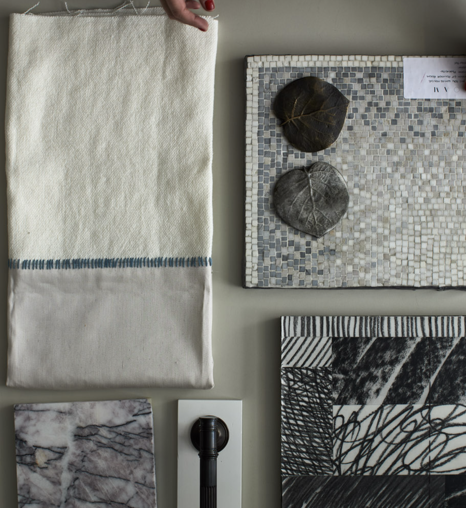 Arrangement of fabric, tile, leaf, and other samples on a table, including white cloth, mosaic tile, black and white patterned paper, and dried leaves.