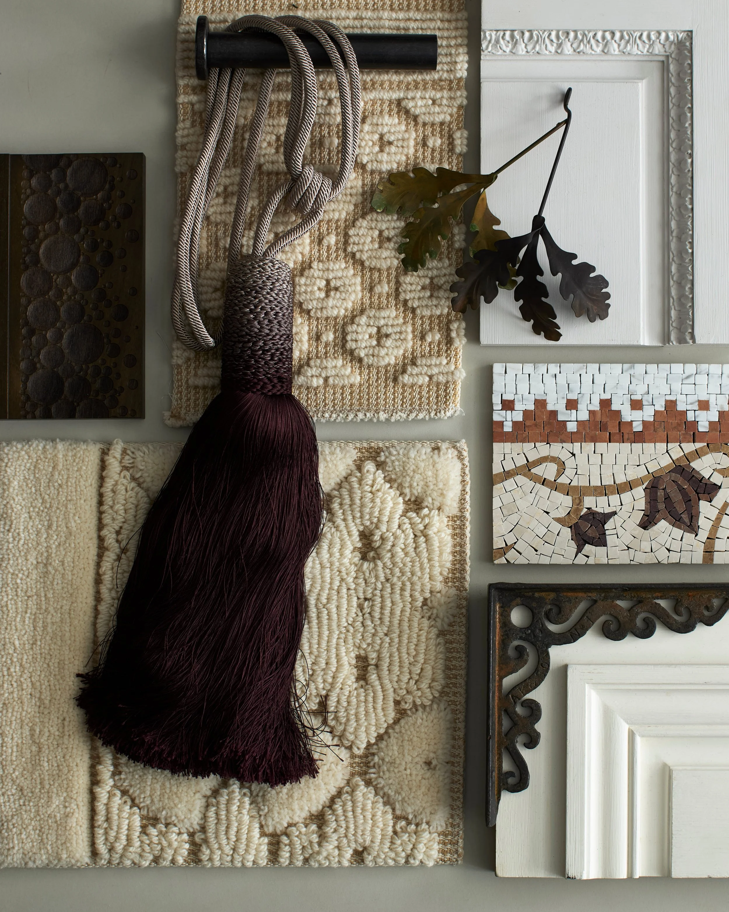 A collection of home decor items including fabric swatches, a tassel, a leaf, and decorative wood and tile pieces arranged on a flat surface.