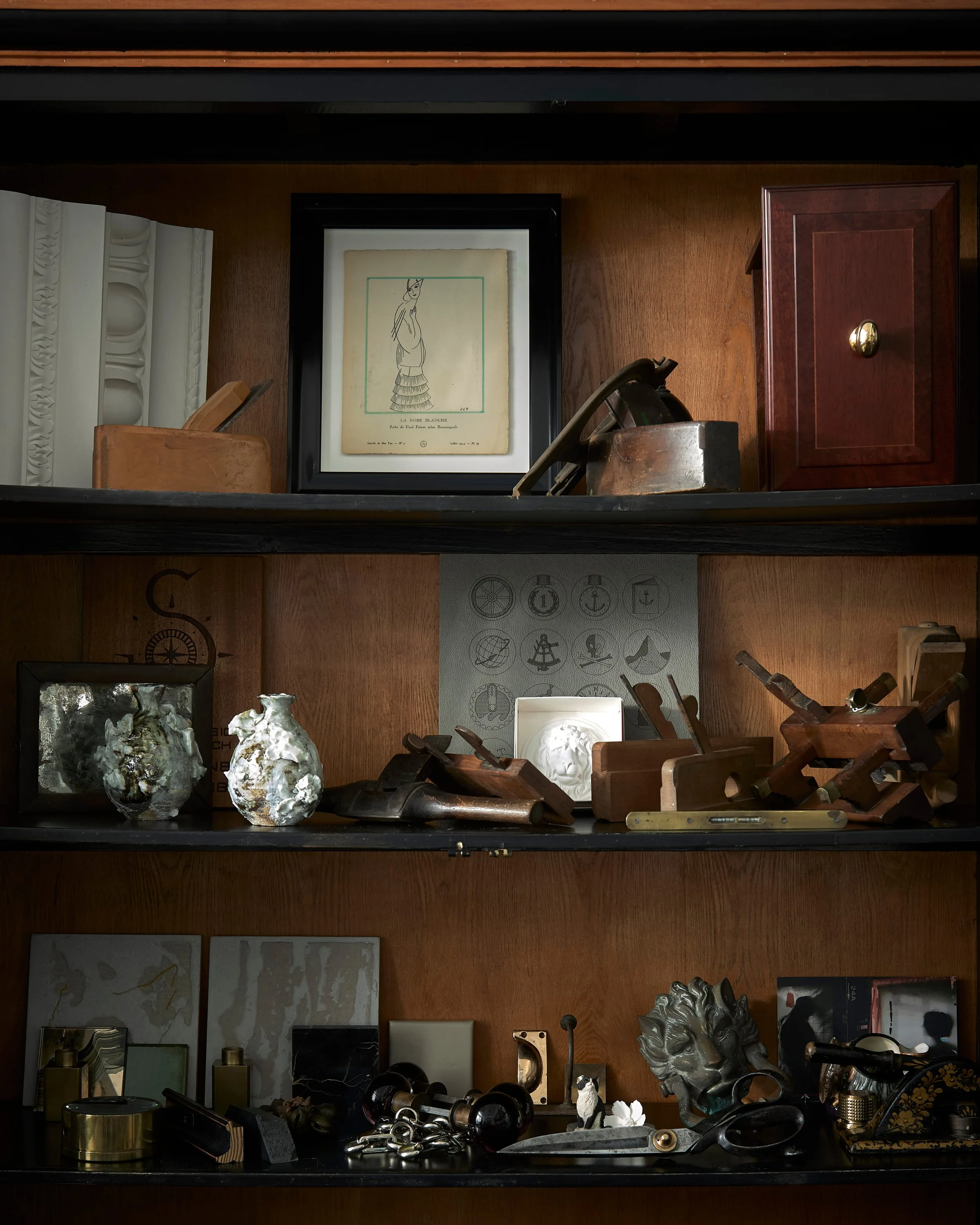 Photos and artworks on wooden shelves, including a framed artistic drawing, sculptures, wooden tools, and miscellaneous decorative objects.