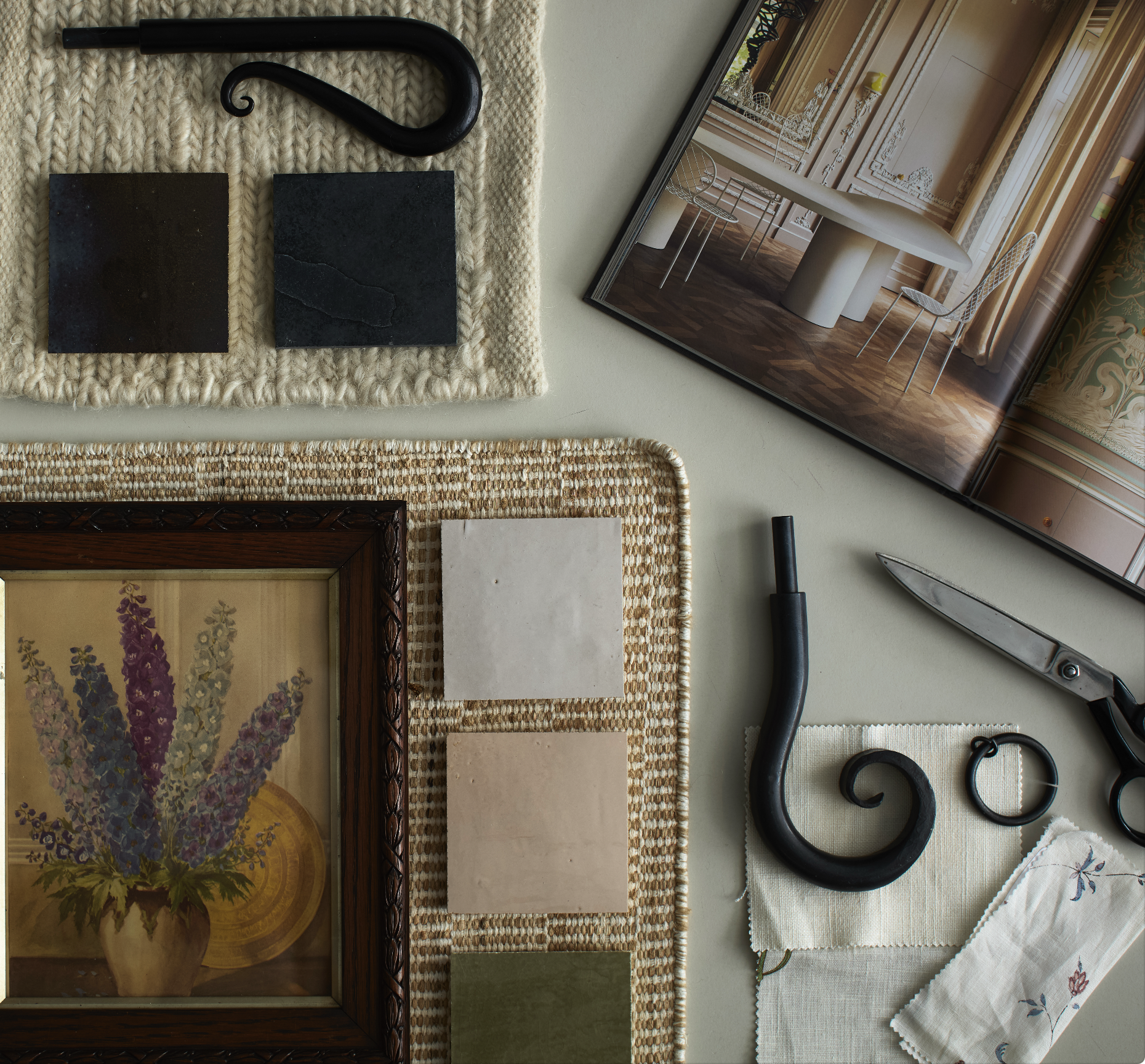 Interior design mood board with tiles, fabric swatches, painting, scissors, and a tablet showing a modern room.