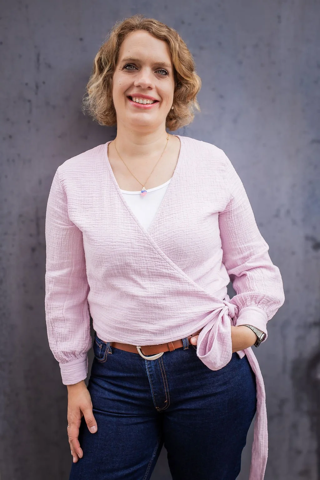 Foto von Meike Hilgemann, frontal, Oberkörper plus Oberschenkel. angelehnt an einer dunklen Wand