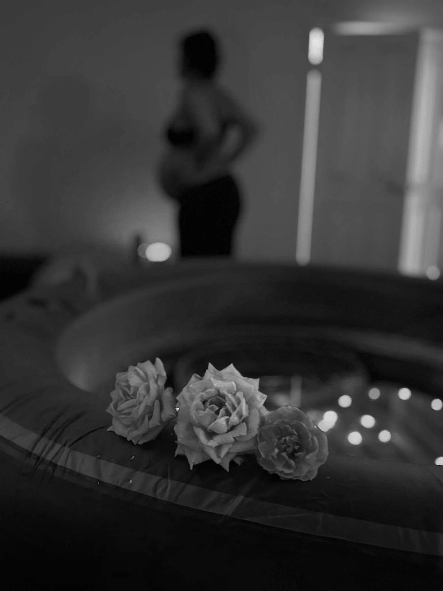 Three flowers resting on a surface with small lights in the background and a blurred person in the distance.