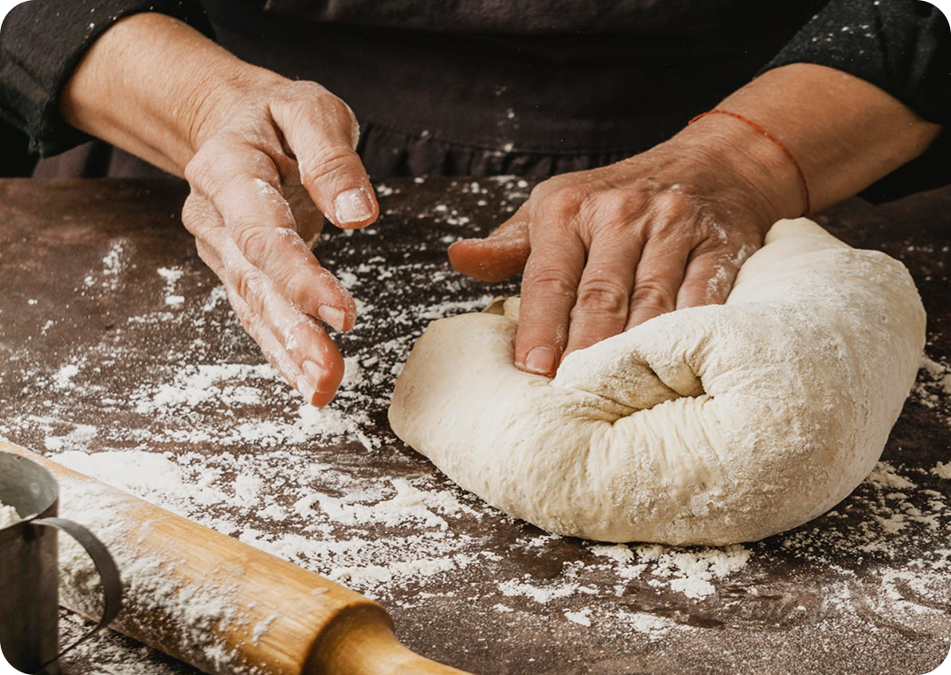 Hands kneading dough on a floured wooden surface.