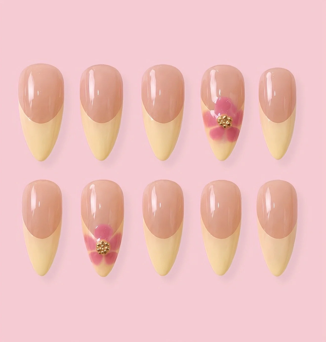 Ten artificial nails with a two-tone pink and beige design, two decorated with pink and gold embellishments, against a pink background.