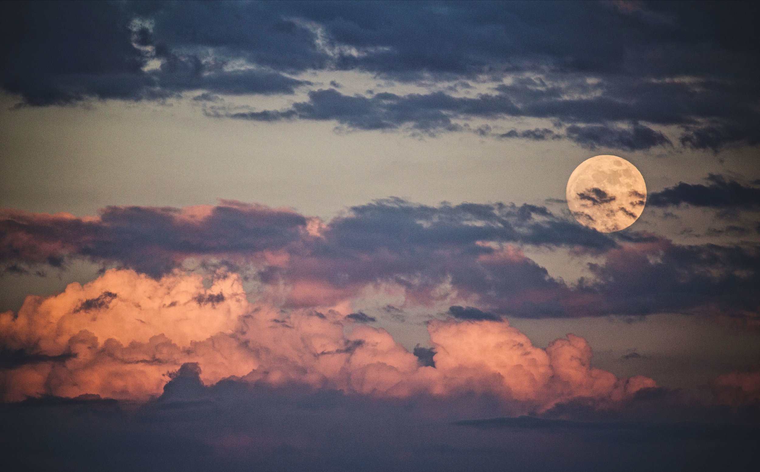The image shows a full moon in a sky filled with dark blue and pink clouds during twilight.