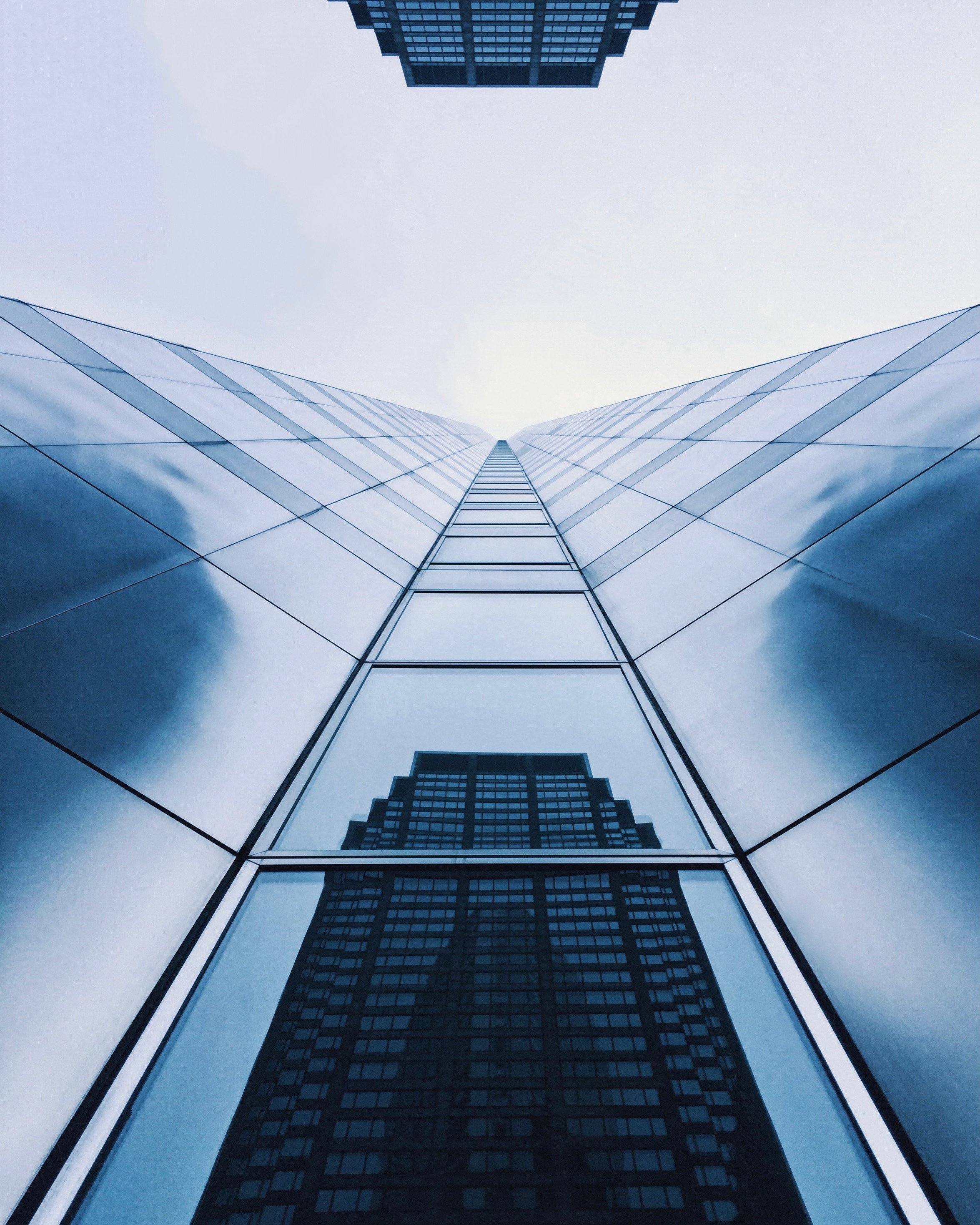 Looking up at tall glass skyscraper buildings with cloudy sky above.