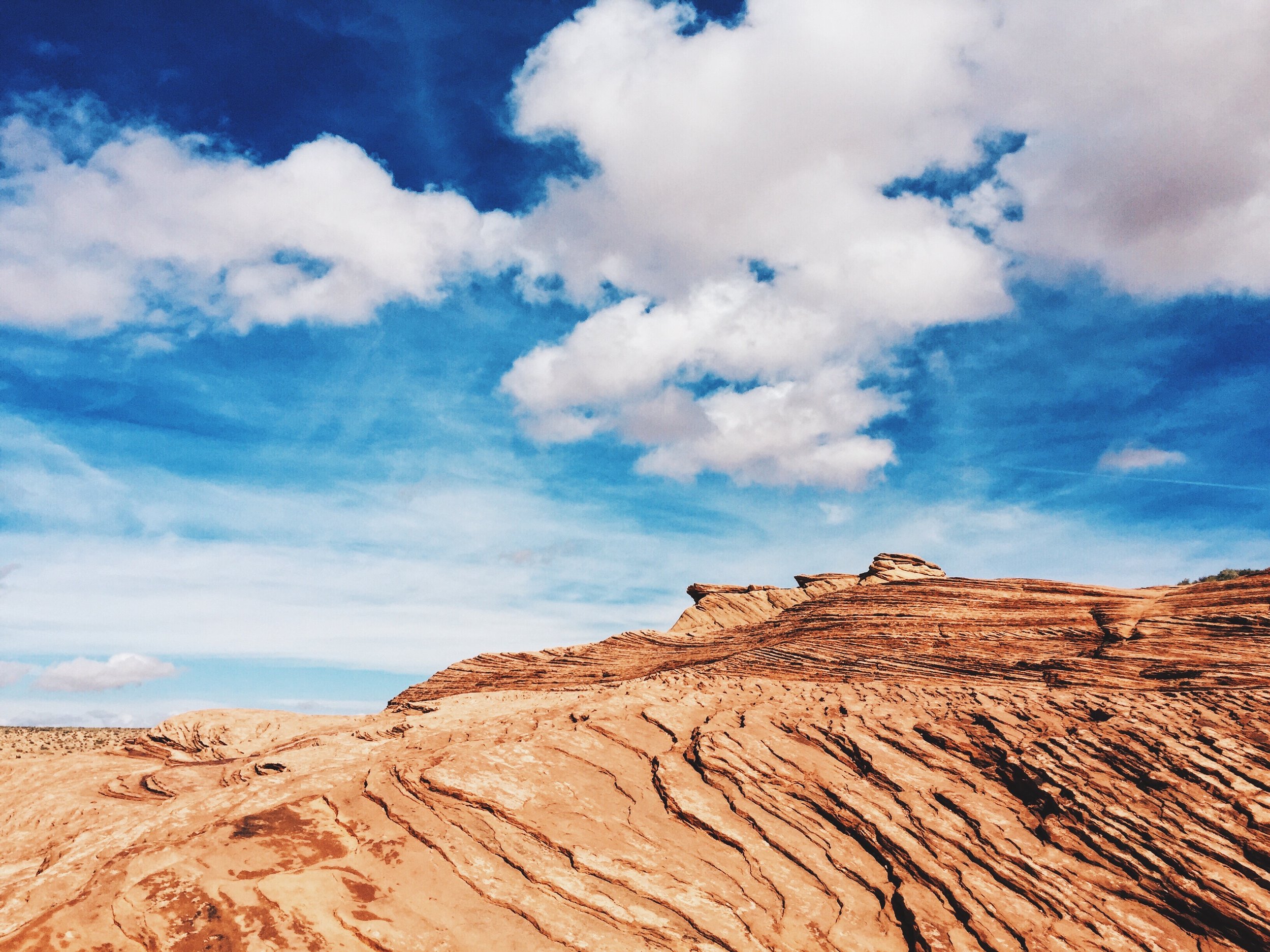 Rock formations with layered patterns in a desert landscape under a partly cloudy blue sky.