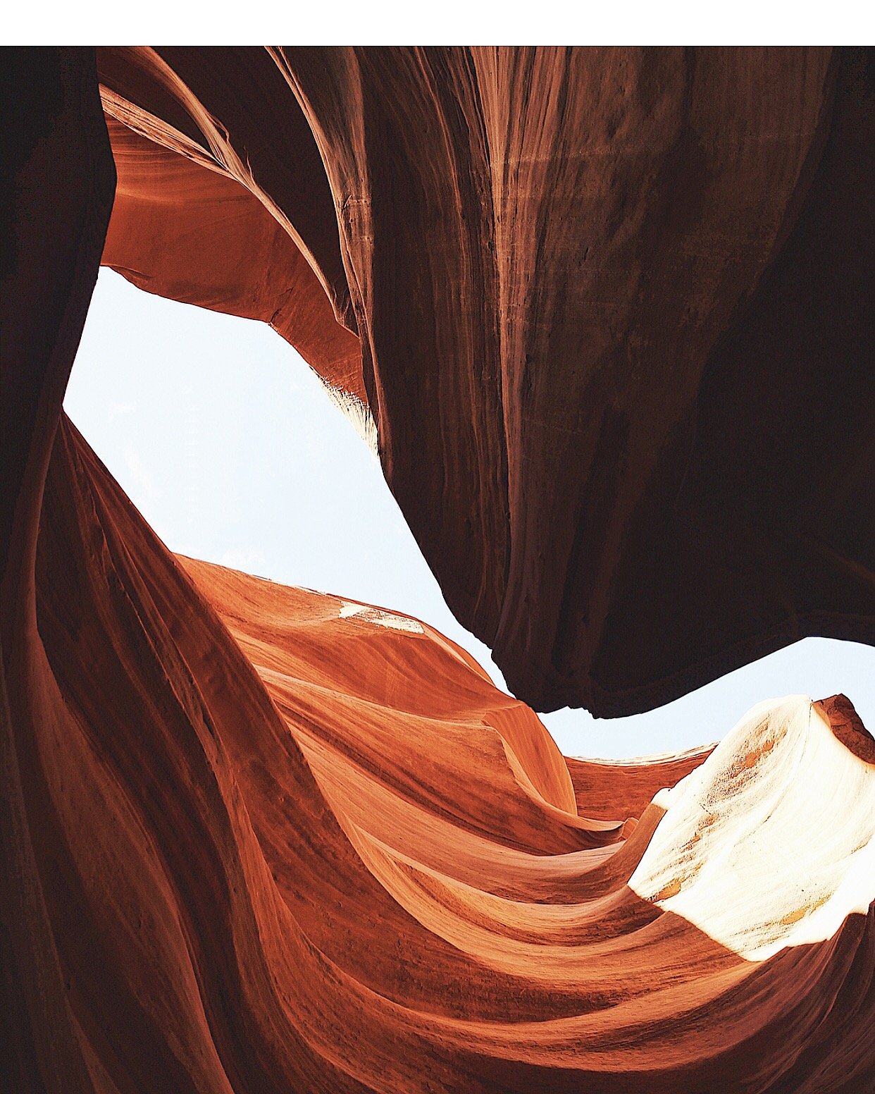 View of slot canyon with red rock walls and a patch of blue sky above