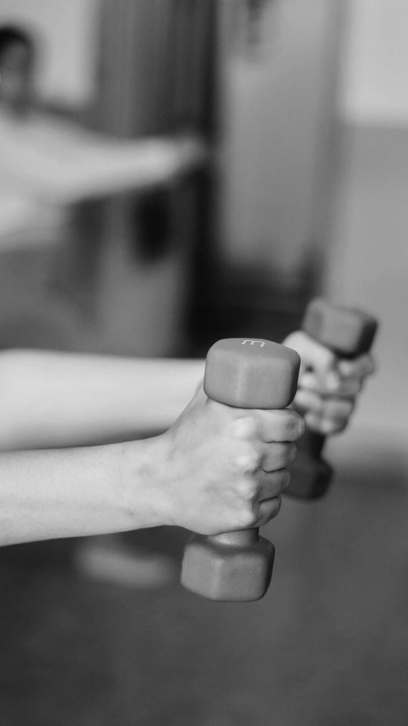 A person holding a dumbbell in each hand, performing a bicep curl exercise. The image is in black and white.