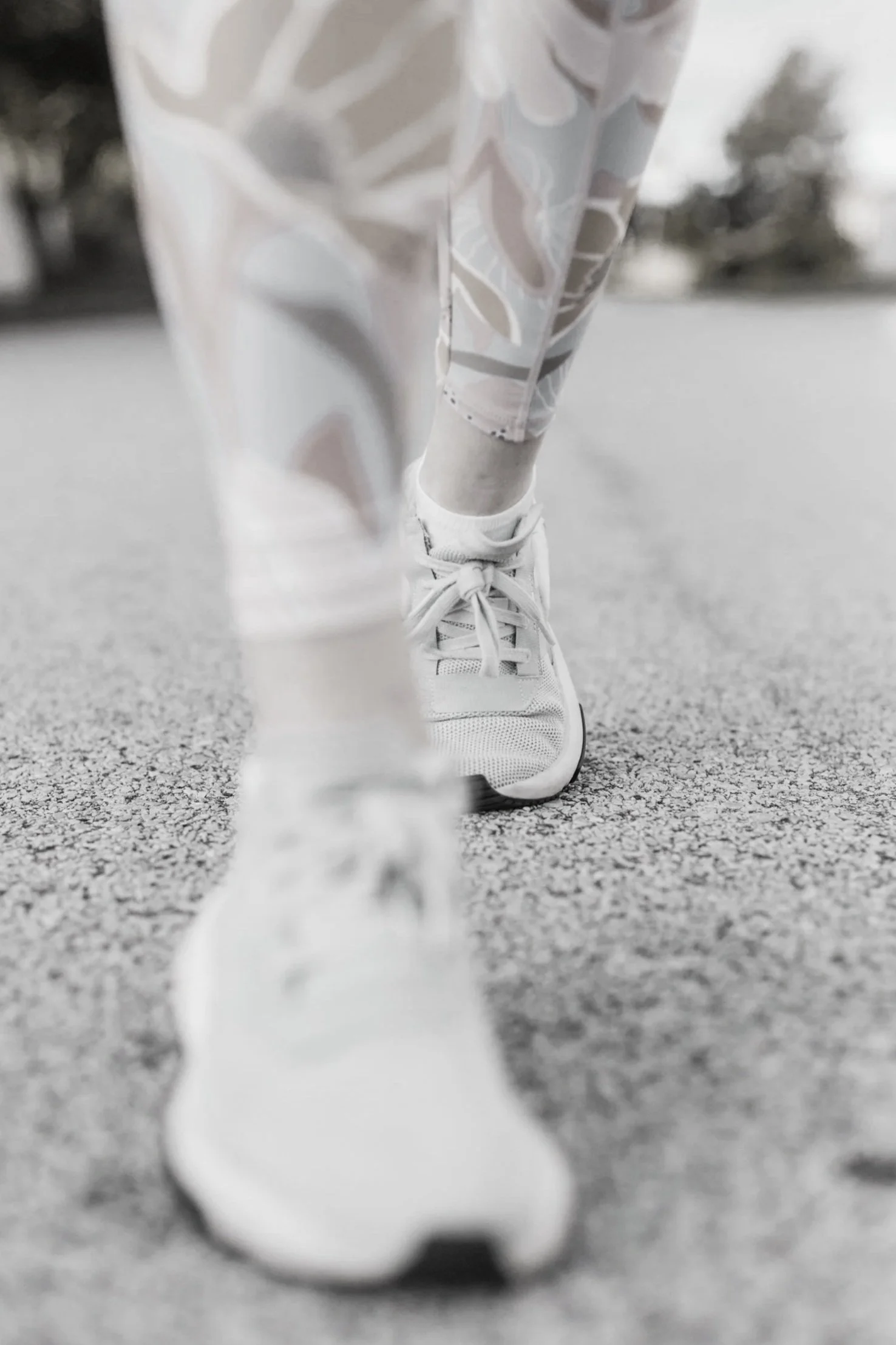 Close-up view of a person walking on pavement, focusing on their white sneaker and patterned leggings, with a blurred background.