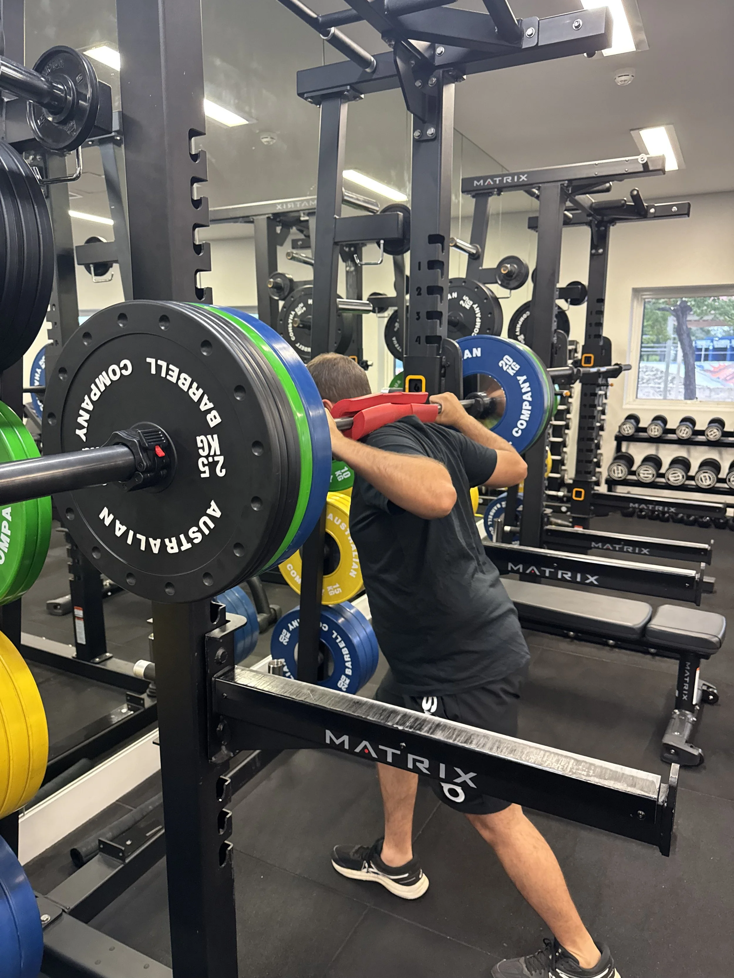 man underneath barbell squat rack with weight plates on in a gym