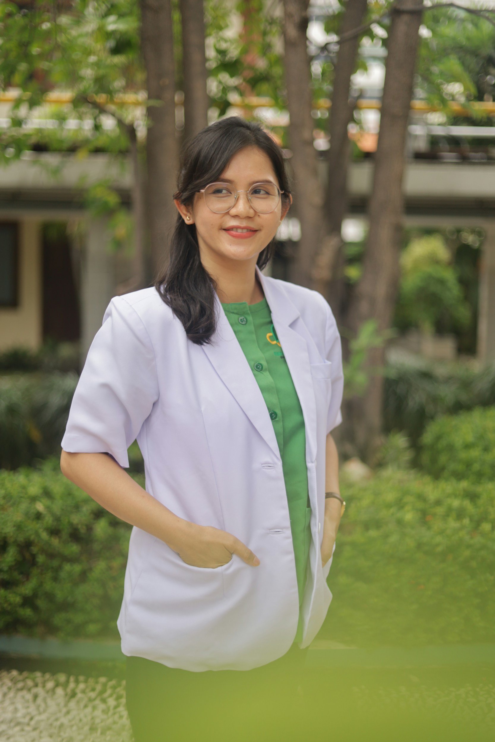 Image of a lady waering a white jacket over a green top, smiling.