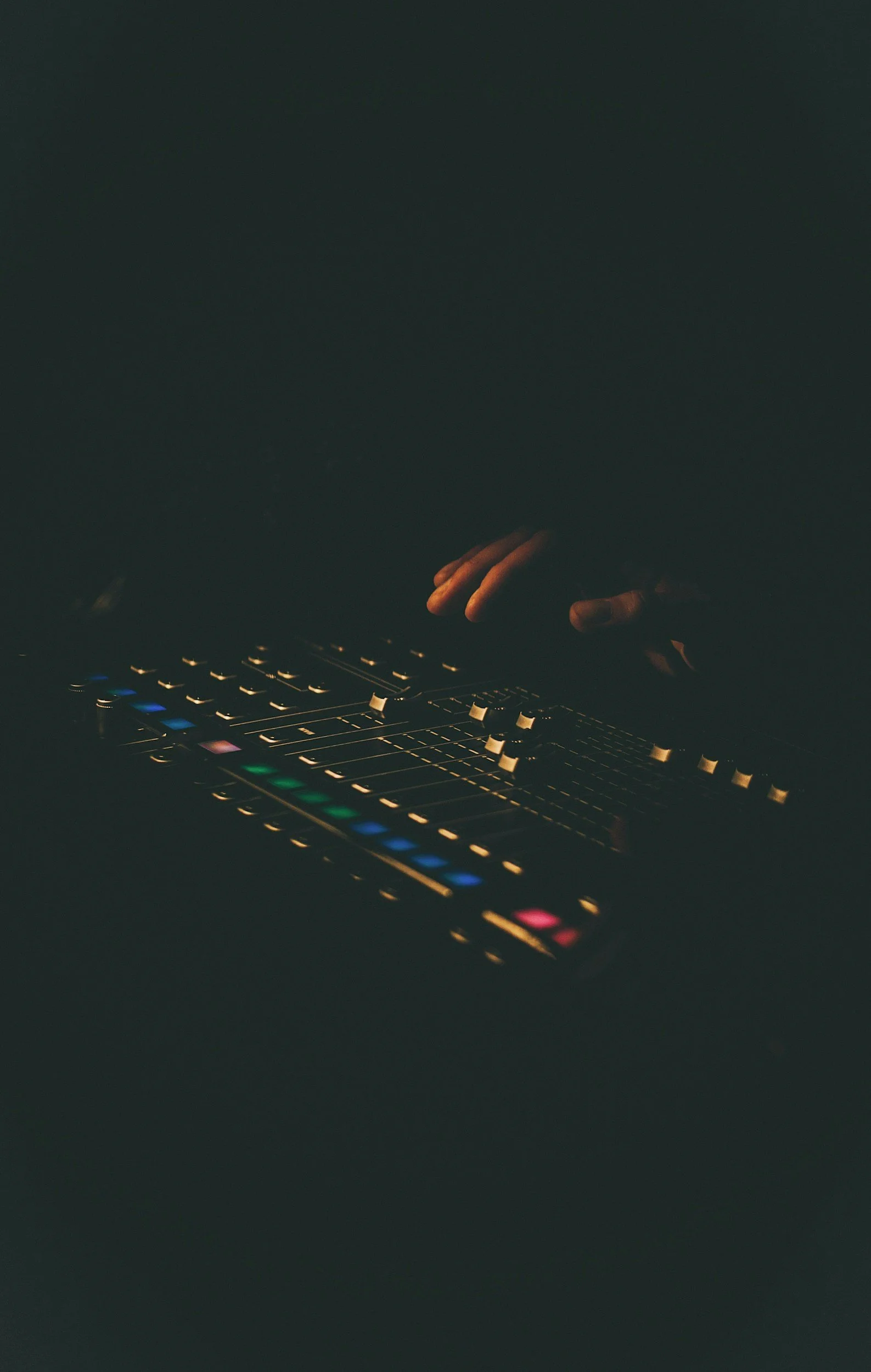Close-up of a person's hand adjusting controls on a music production equipment in a dark environment with colorful LED lights.