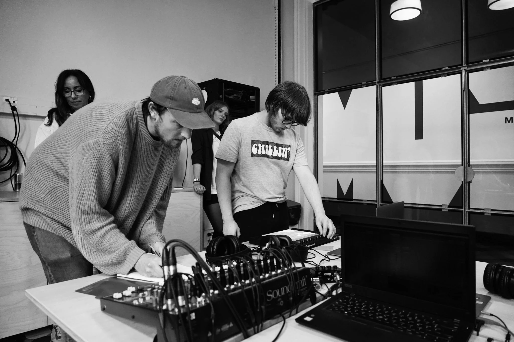 Group of people in a music studio using electronic music equipment, with computer and headphones on the table.