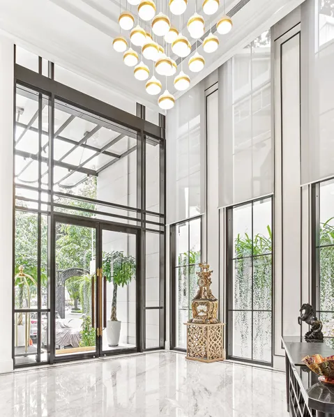 Interior view of a modern entrance with large glass doors, tall windows, high ceiling, and a chandelier with multiple circular lights.