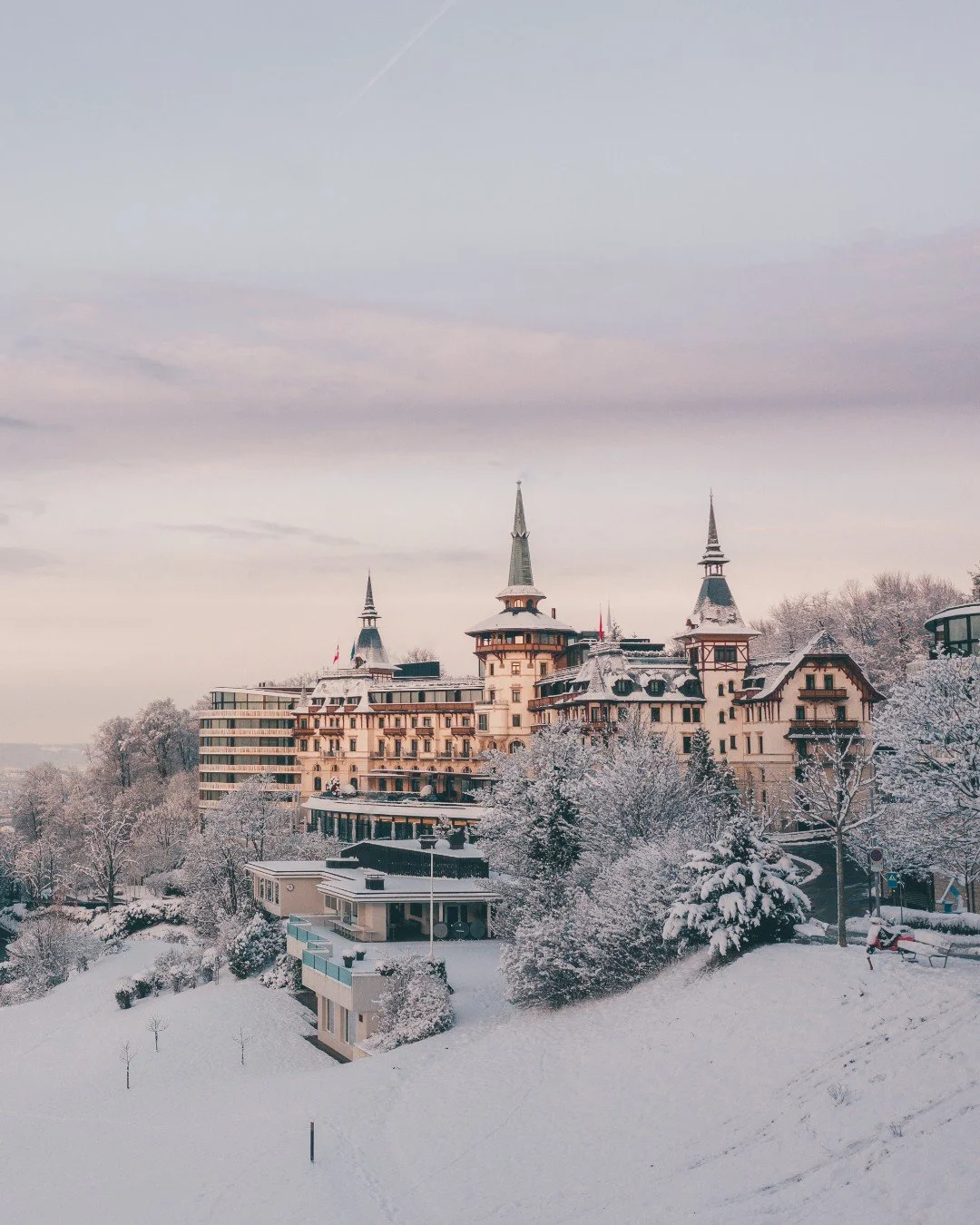 A large snow-covered castle or hotel with multiple spires, surrounded by snow-covered trees and a snowy landscape.