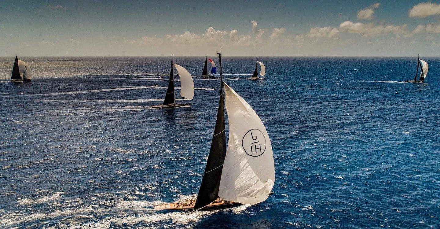 Multiple sailboats racing on open water with blue sky and clouds above.