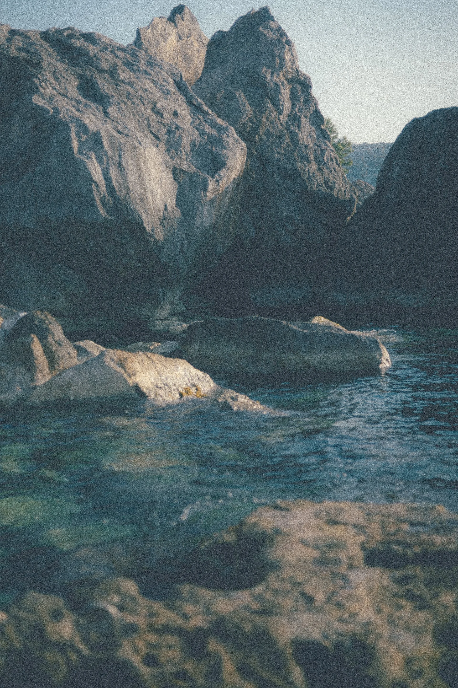 Large rocks and boulders near a calm river with a mountain backdrop.