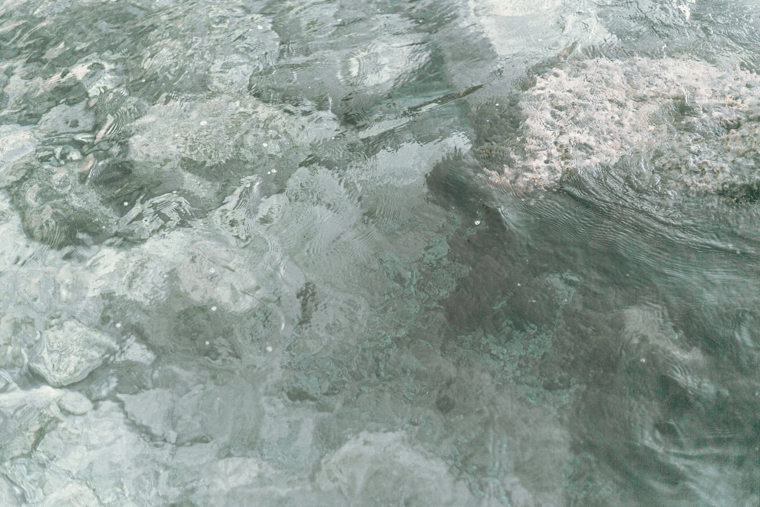 Underwater view of clear water with rocks and pebbles visible beneath the surface.