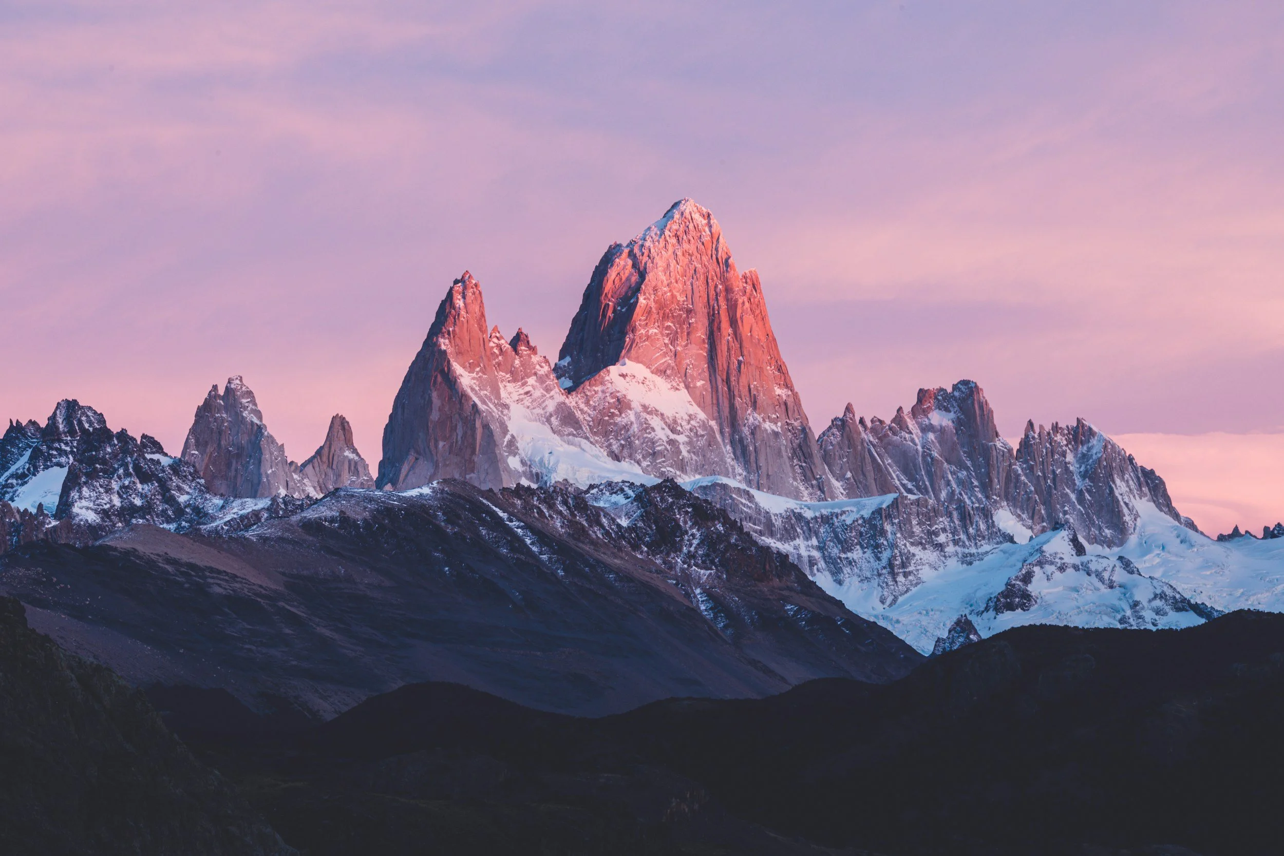 Snow-capped mountain peaks during sunset with pink and purple sky.