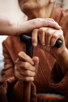 Close-up of one person helping another elderly person hold a walking cane.