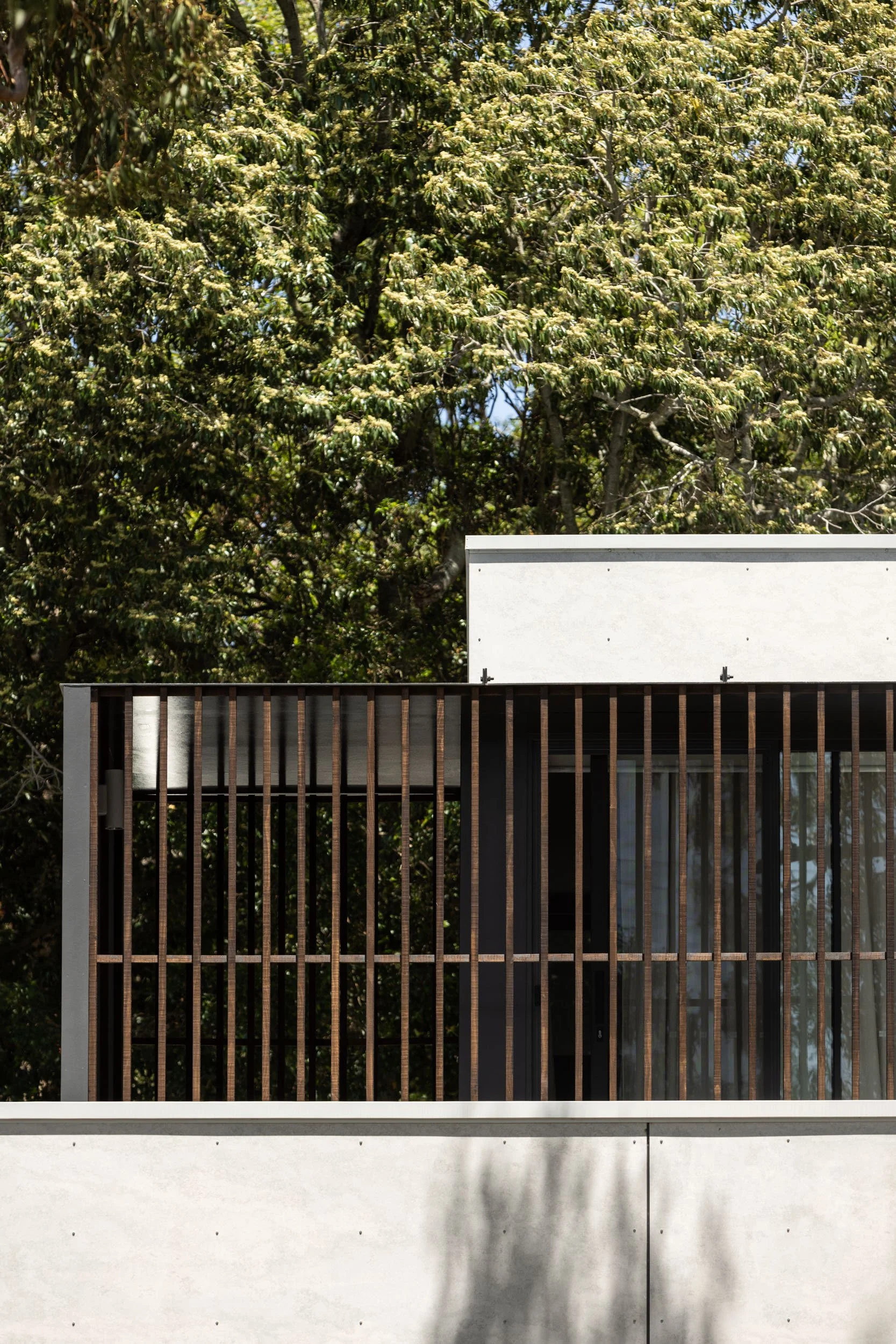 Modern building with vertical wooden slats on the balcony railing, against a background of lush green trees and a clear blue sky.