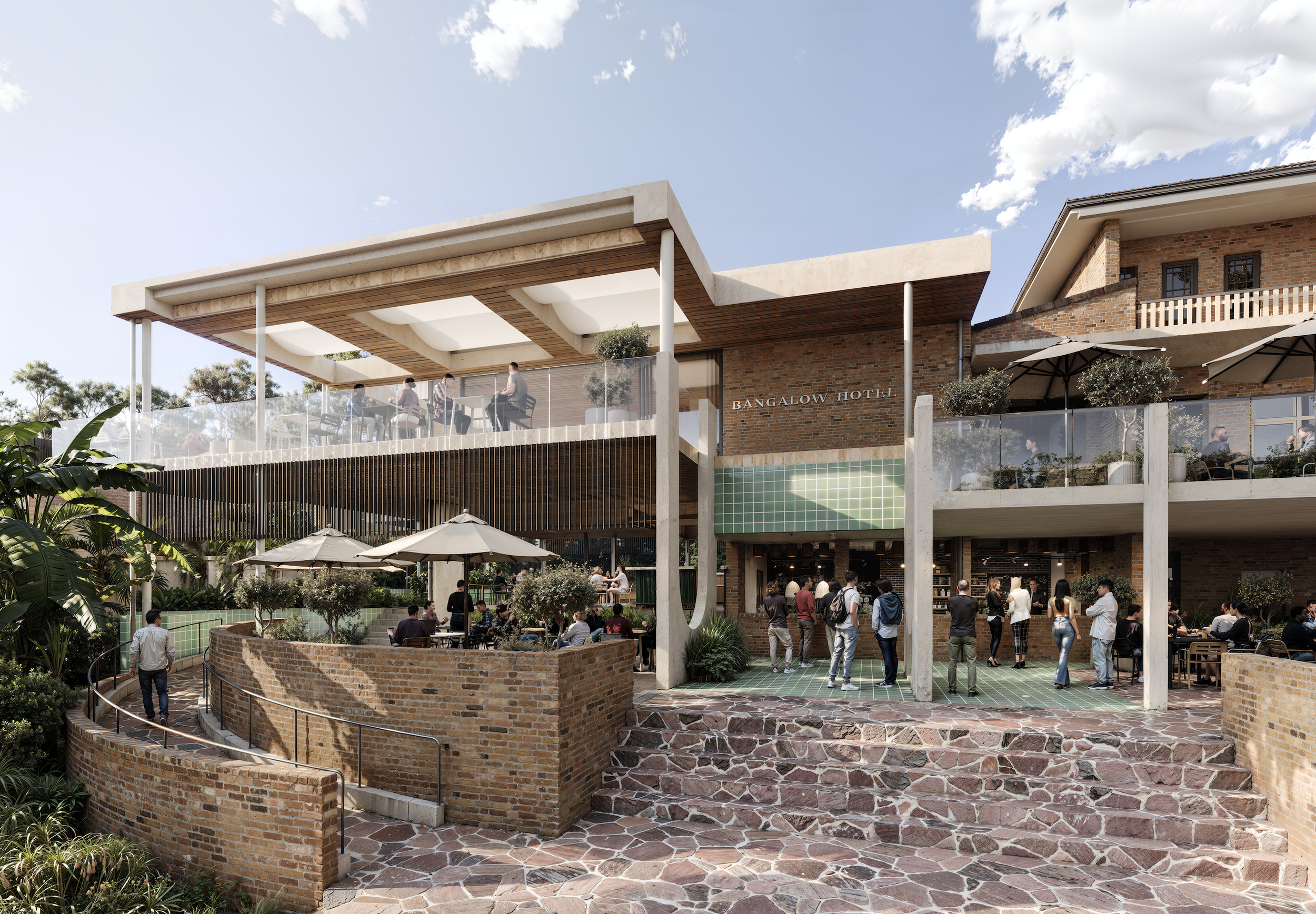 Outdoor seating area at the Bangalow Hotel with people gathered, brick and concrete building, trees, umbrellas, and a clear blue sky.