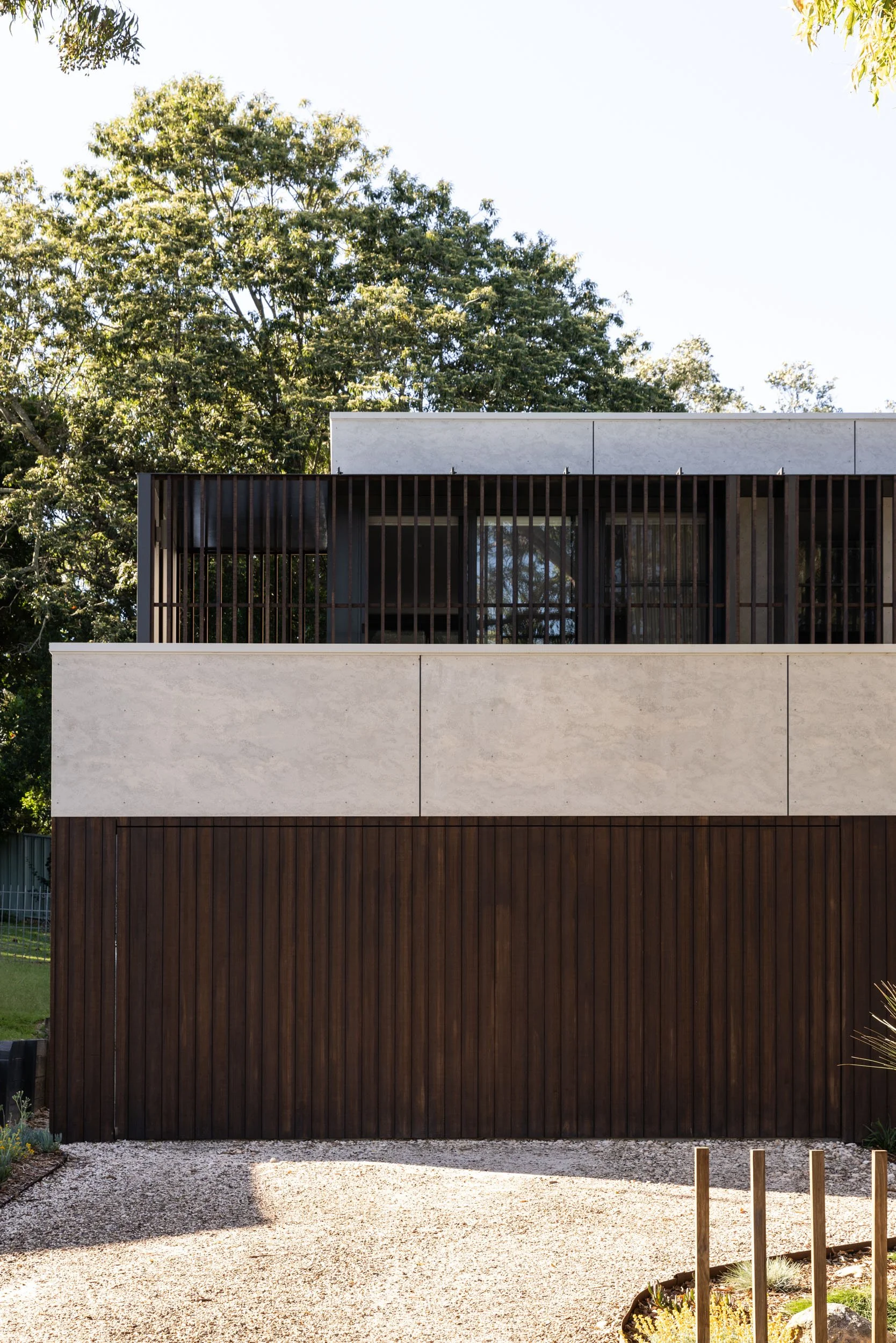 Modern house with a combination of white concrete and dark wood exterior, large windows, and a garden in front, surrounded by trees