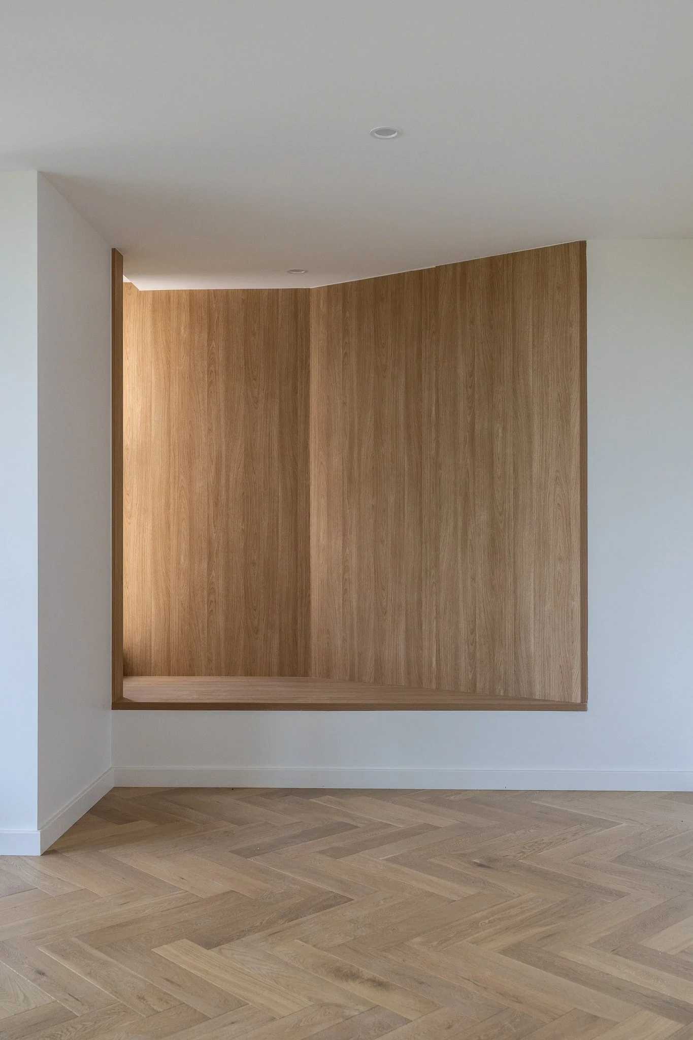 Empty room with white walls, a wooden partition, light wood herringbone flooring, and a circular ceiling light.