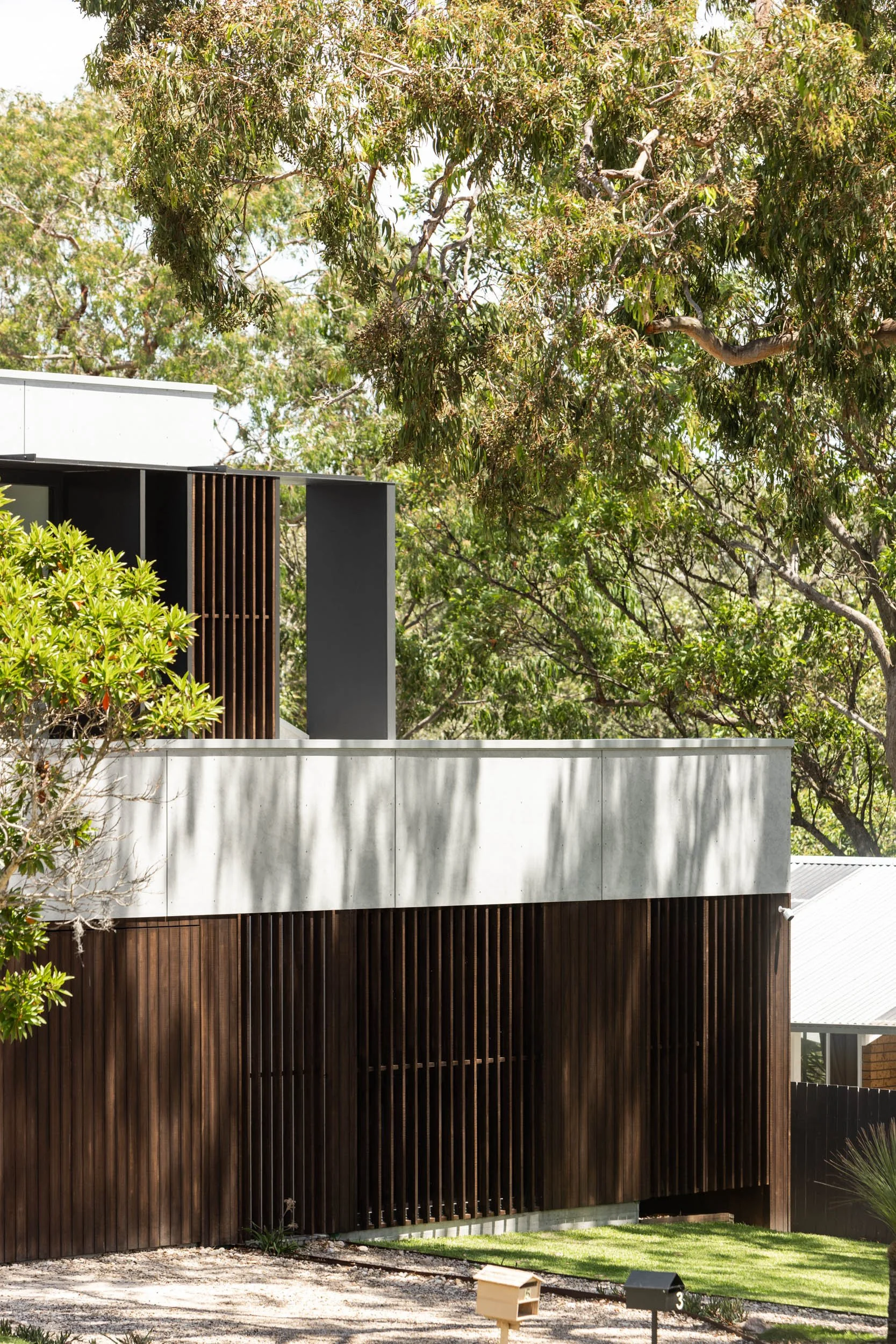 Modern house with white and dark wood exterior, surrounded by trees and a small lawn.
