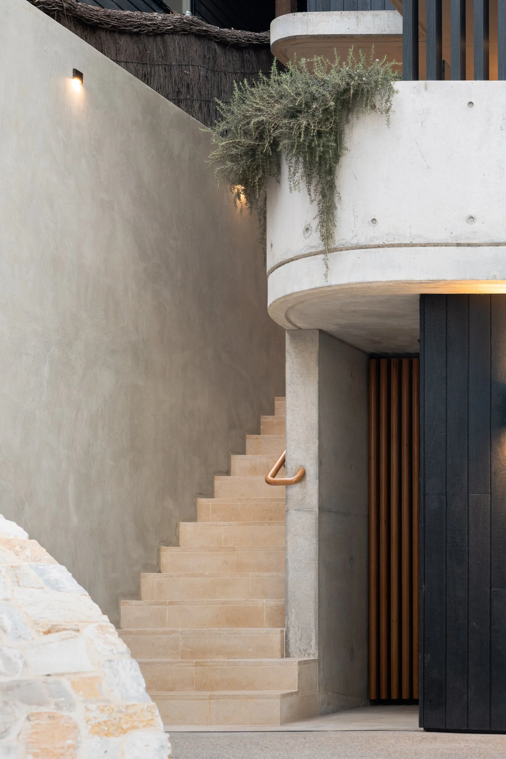 Modern interior staircase with beige stone steps, a concrete wall, and wooden and black panel accents.