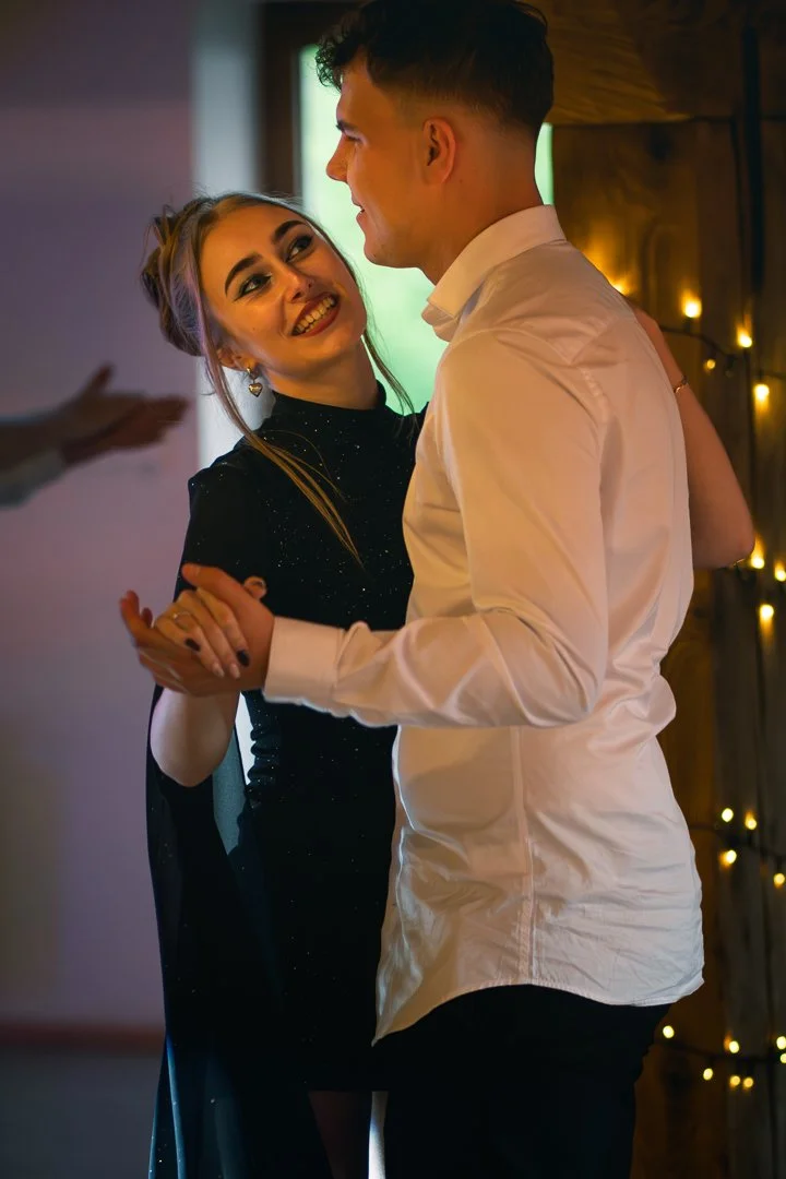 A couple dancing closely together indoors, with warm lighting and string lights in the background.