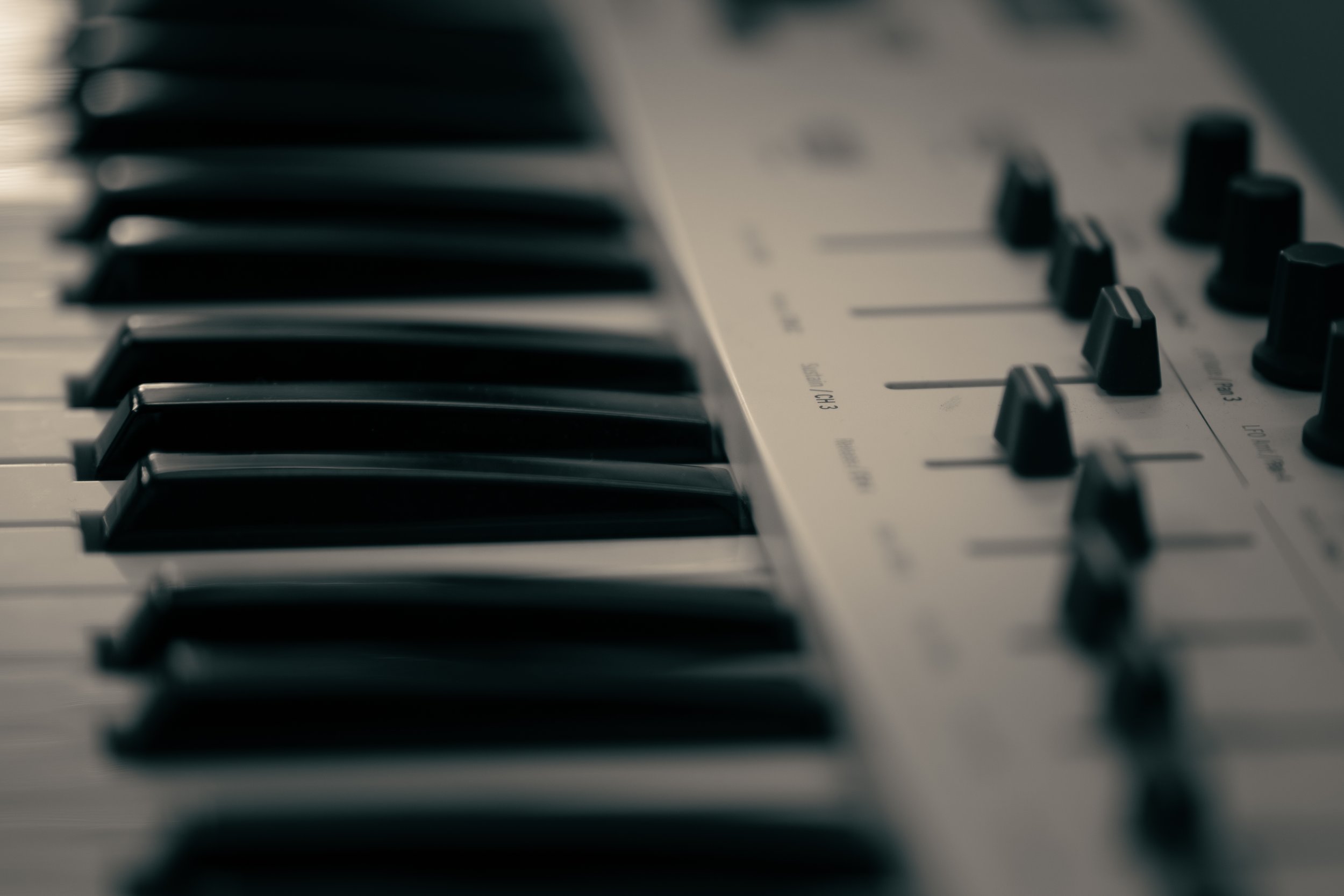 Close-up of a keyboard and audio mixing console with black and white keys and control knobs.