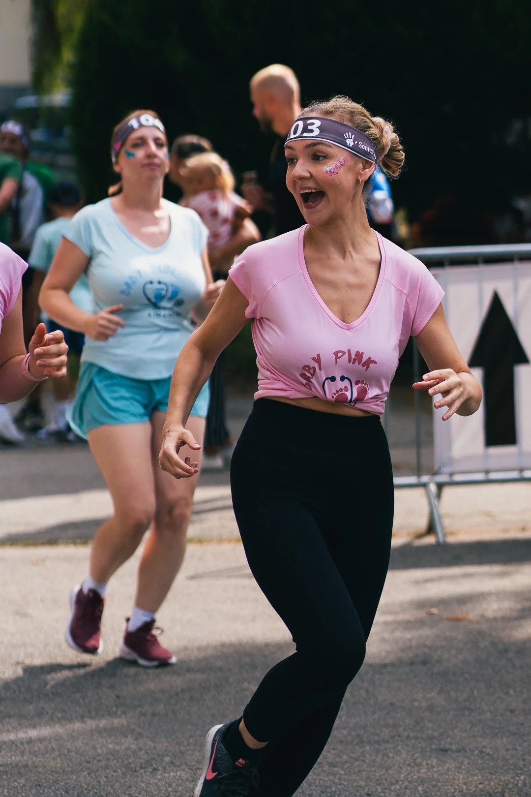 Women participating in a fun run, wearing athletic clothes, headbands, and face paint, jogging on the street during daytime.