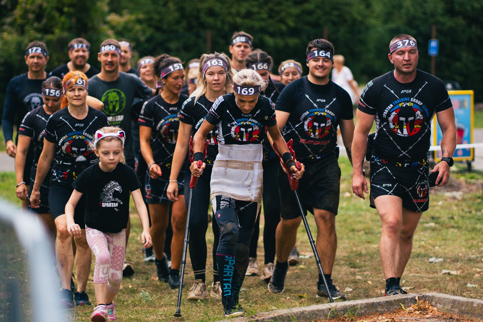 A group of people participating in an outdoor fitness event, with some wearing matching shirts and a young girl dressed with a cat headband walking in front.