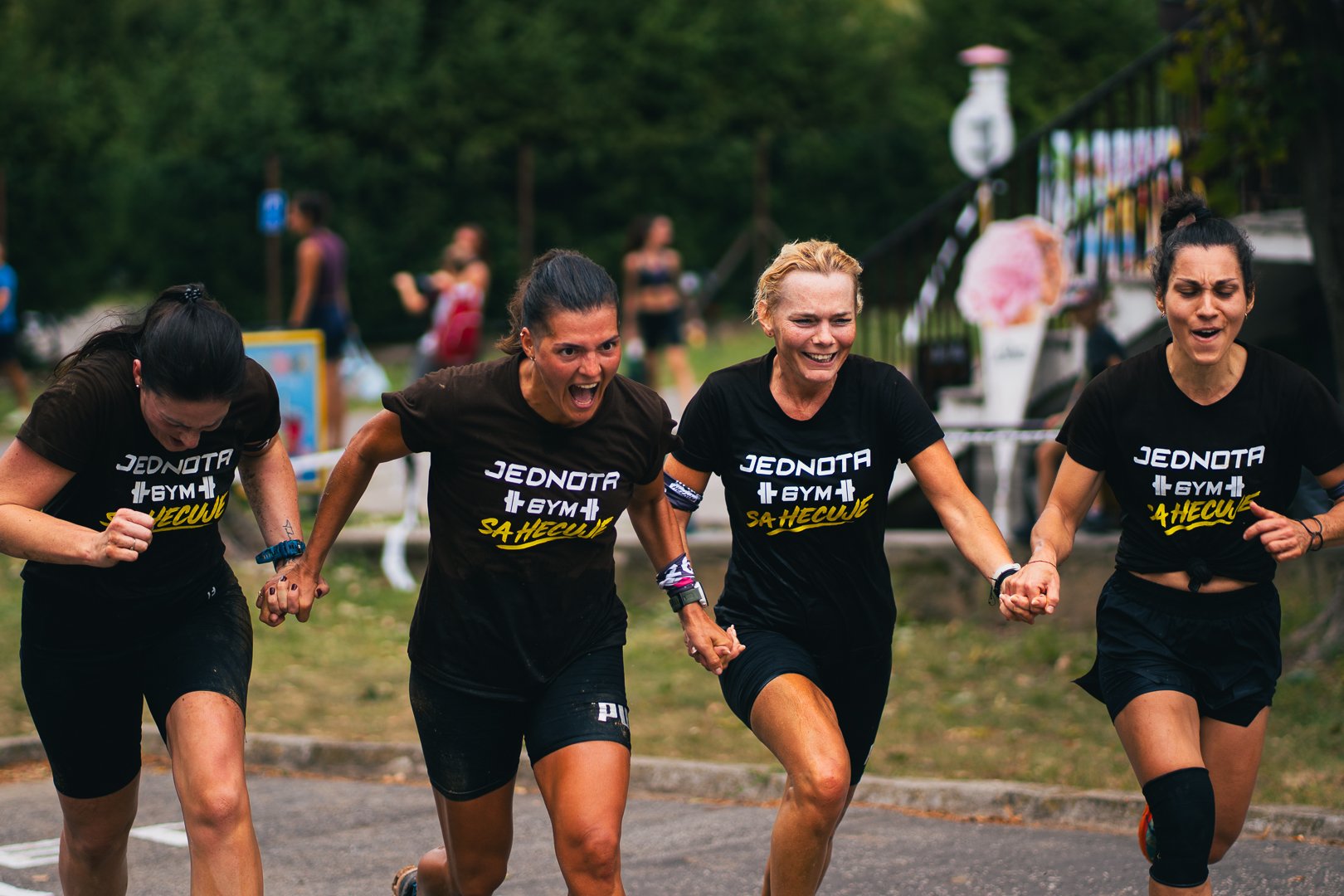 Four women in black t-shirts holding hands and running outdoors during a race or event.